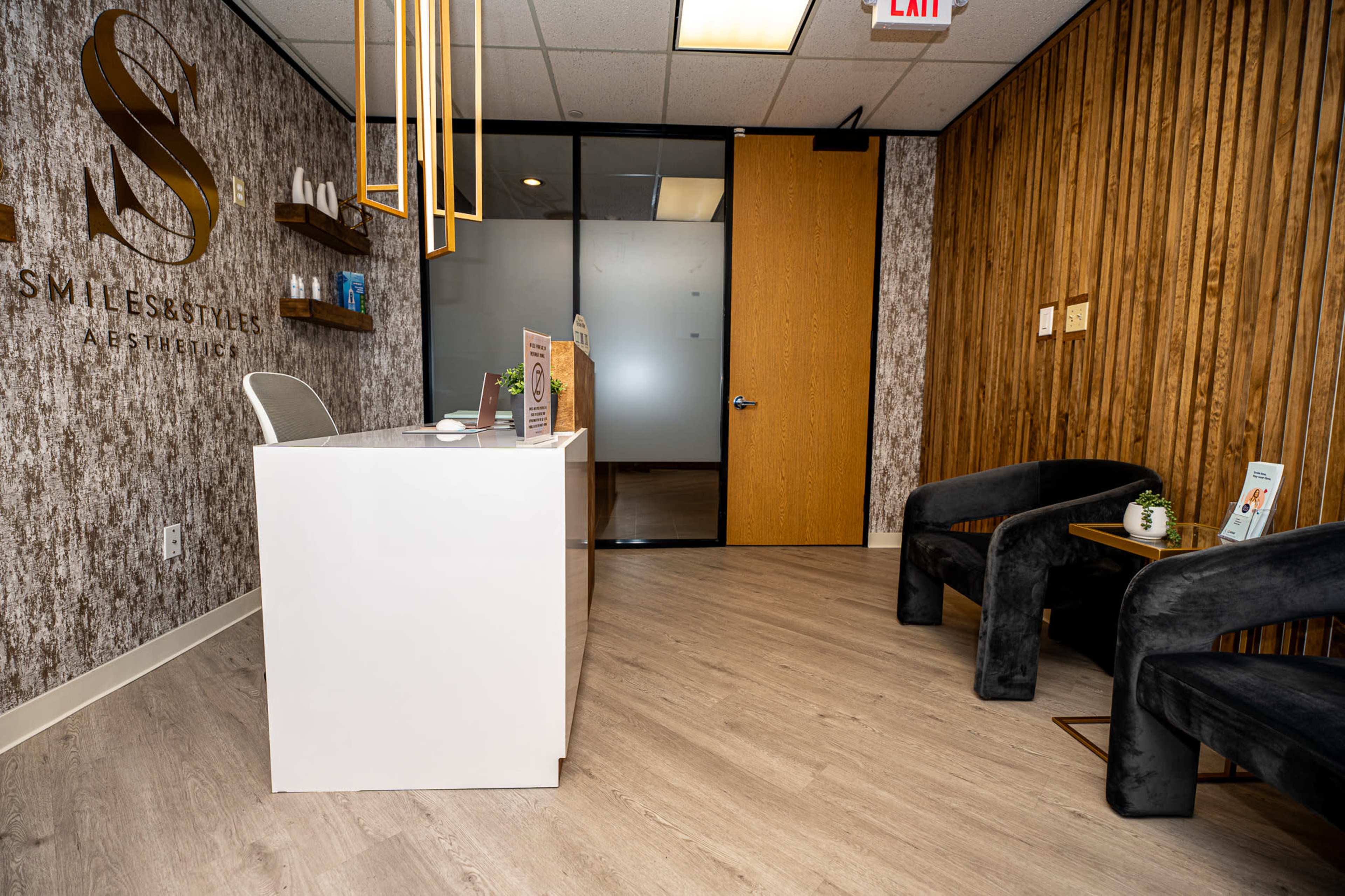 The image shows a modern reception area with a white desk, wooden accent walls, and two black chairs.