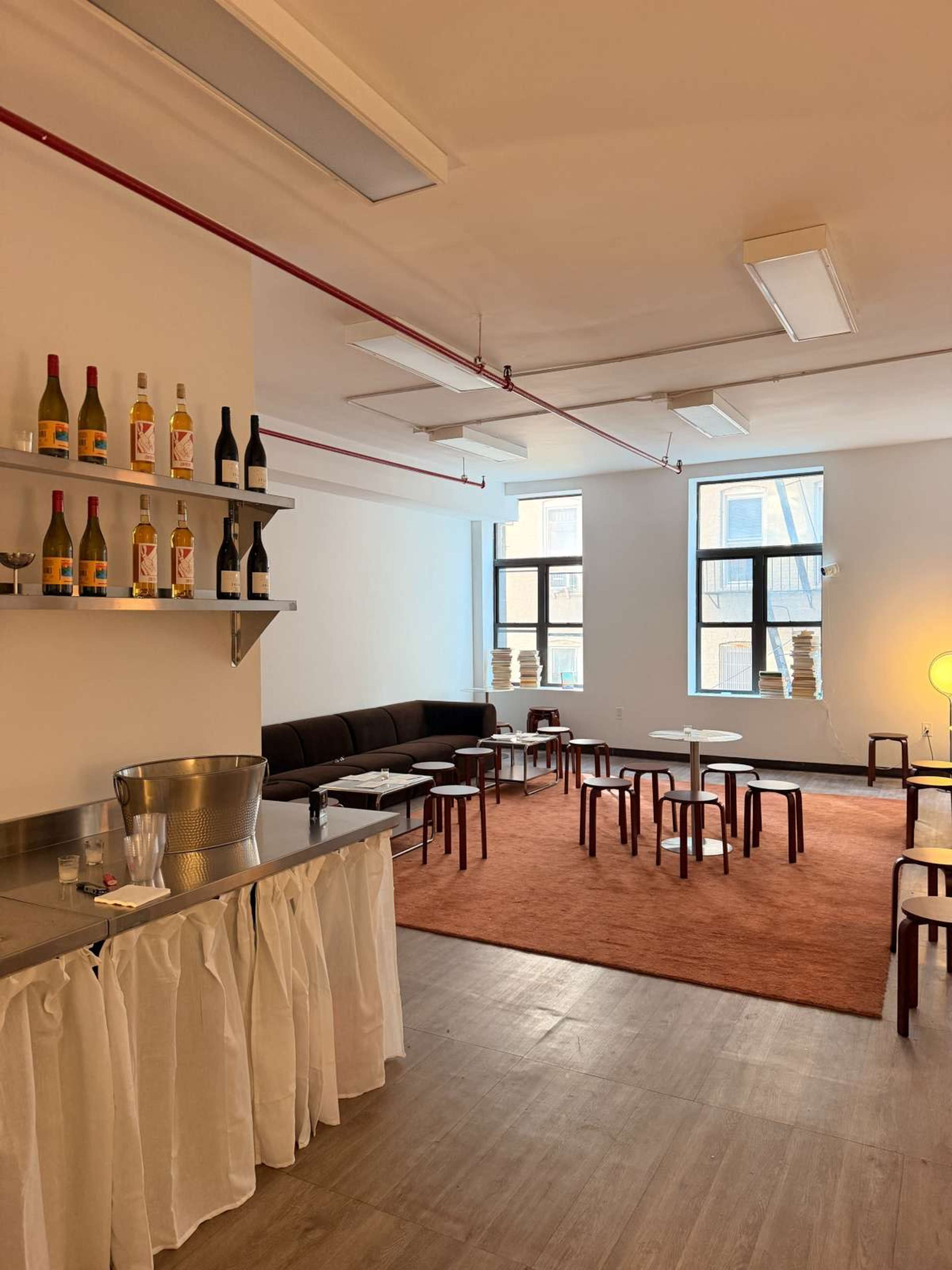 The image shows a modern, minimalistic lounge area with a bar, seating arrangements, and large windows.