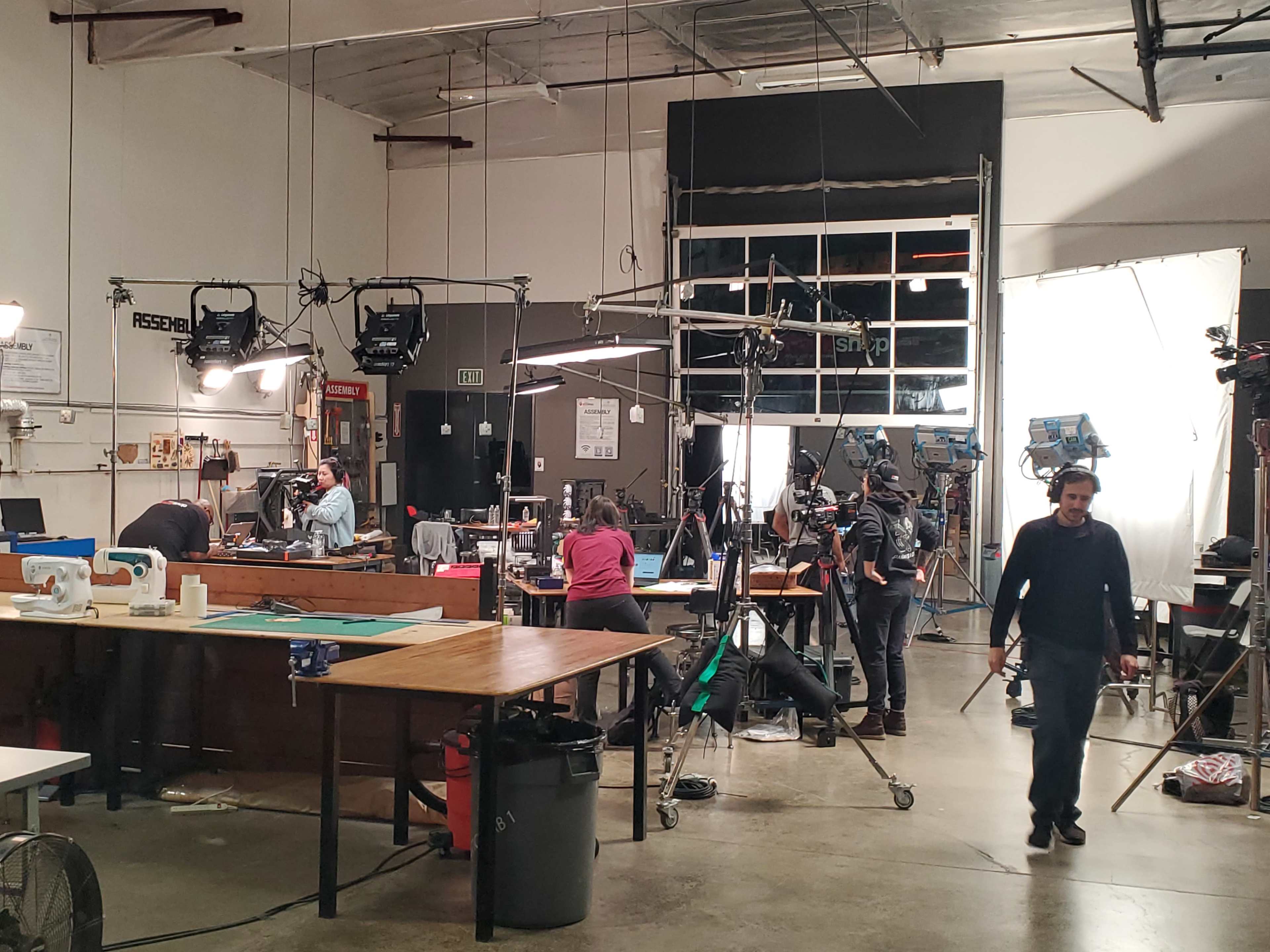 A busy film set with multiple cameras and lighting equipment in use, featuring crew members working on various tasks.