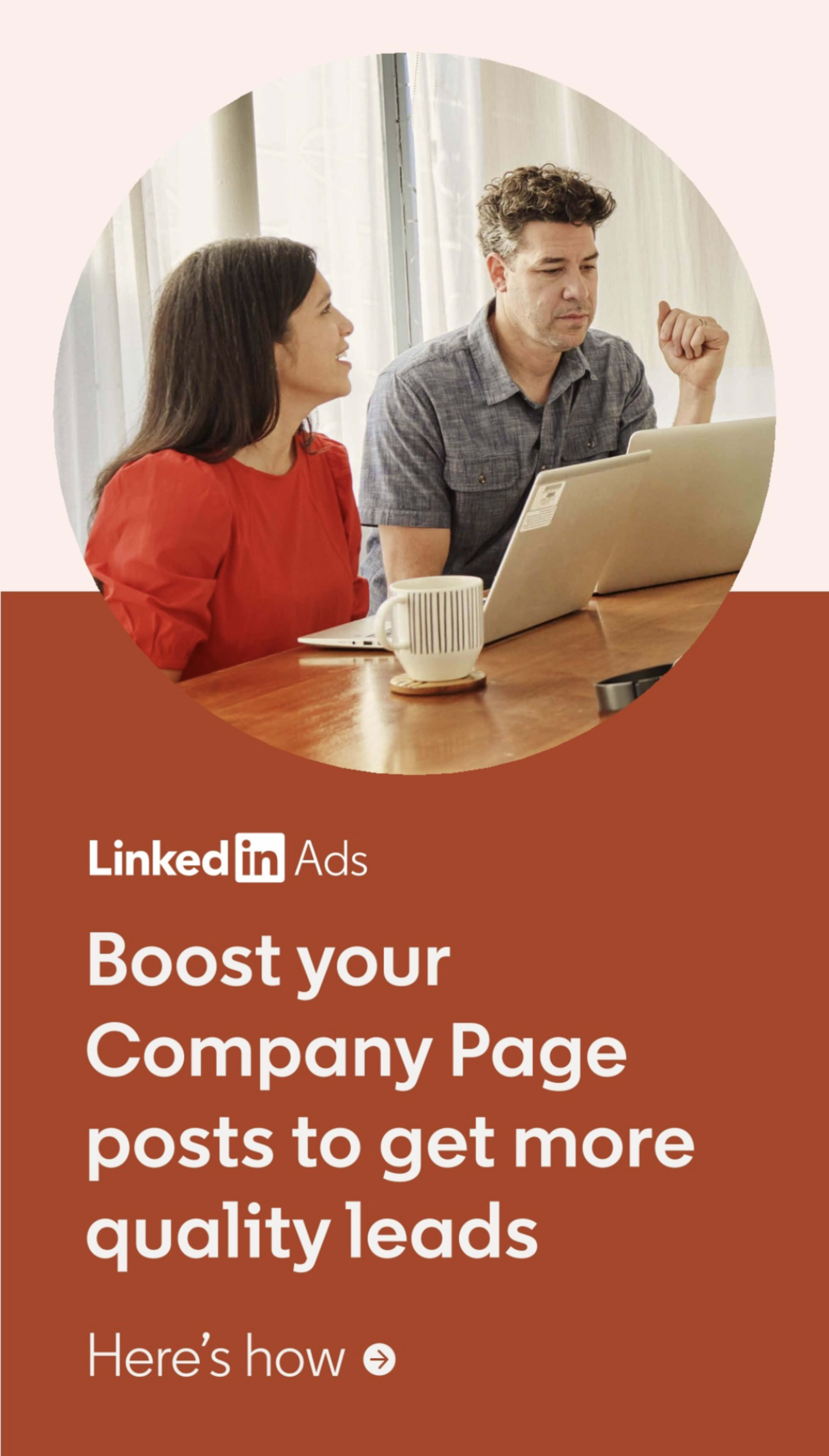A man and a woman are sitting at a table, looking at a laptop while discussing LinkedIn Ads aimed at boosting company page posts.