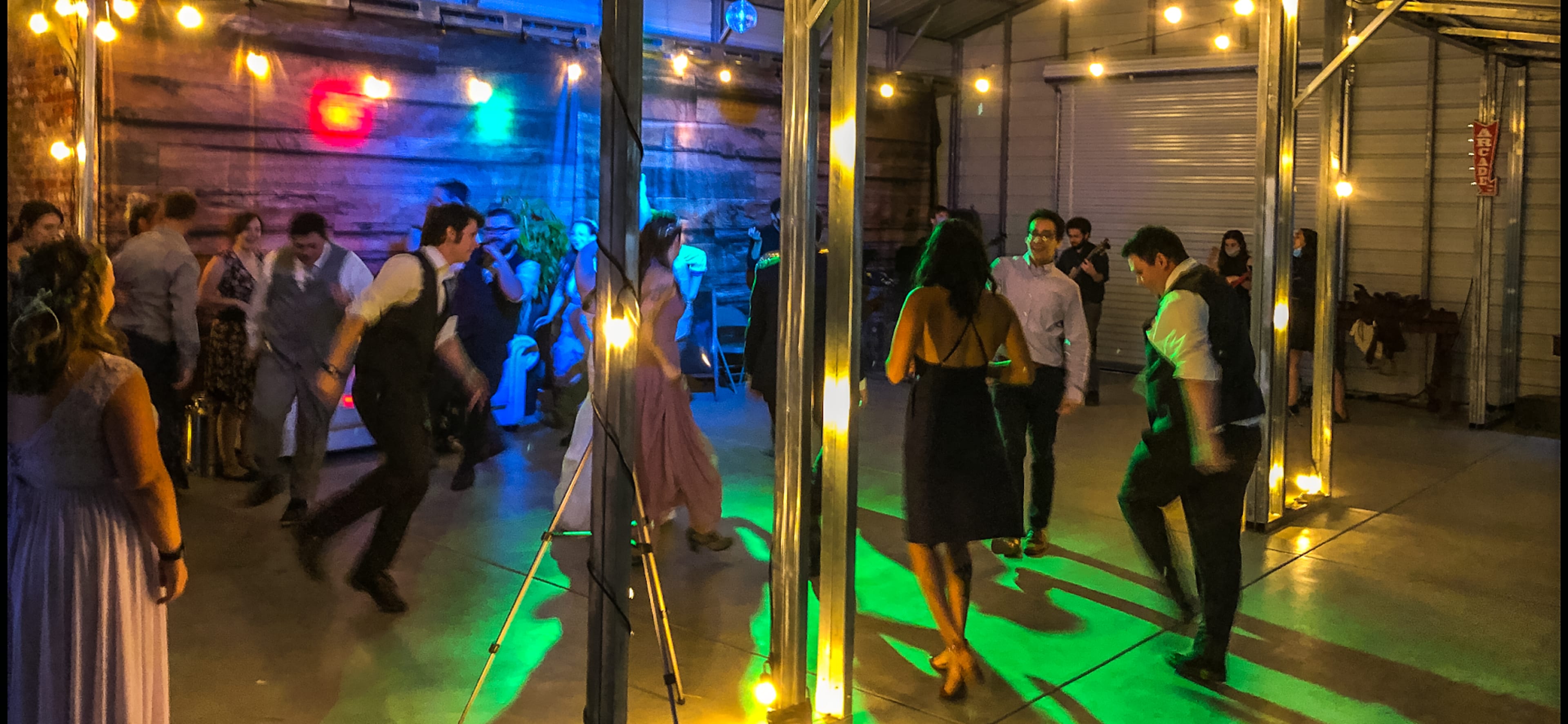A group of people dances under string lights in a large indoor space with colorful lighting.