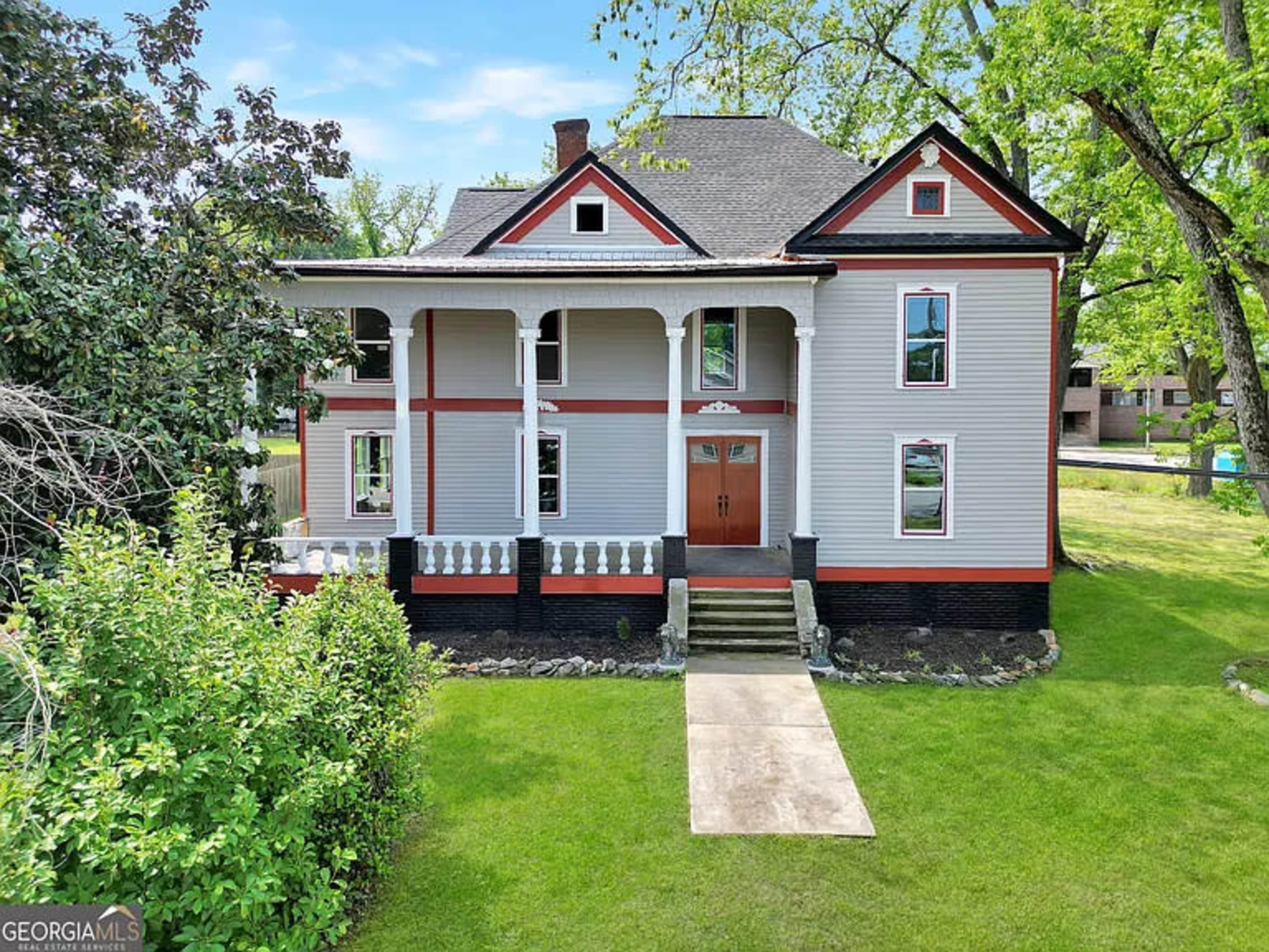 The image shows a two-story historical house with a columned porch and a neatly landscaped front yard.