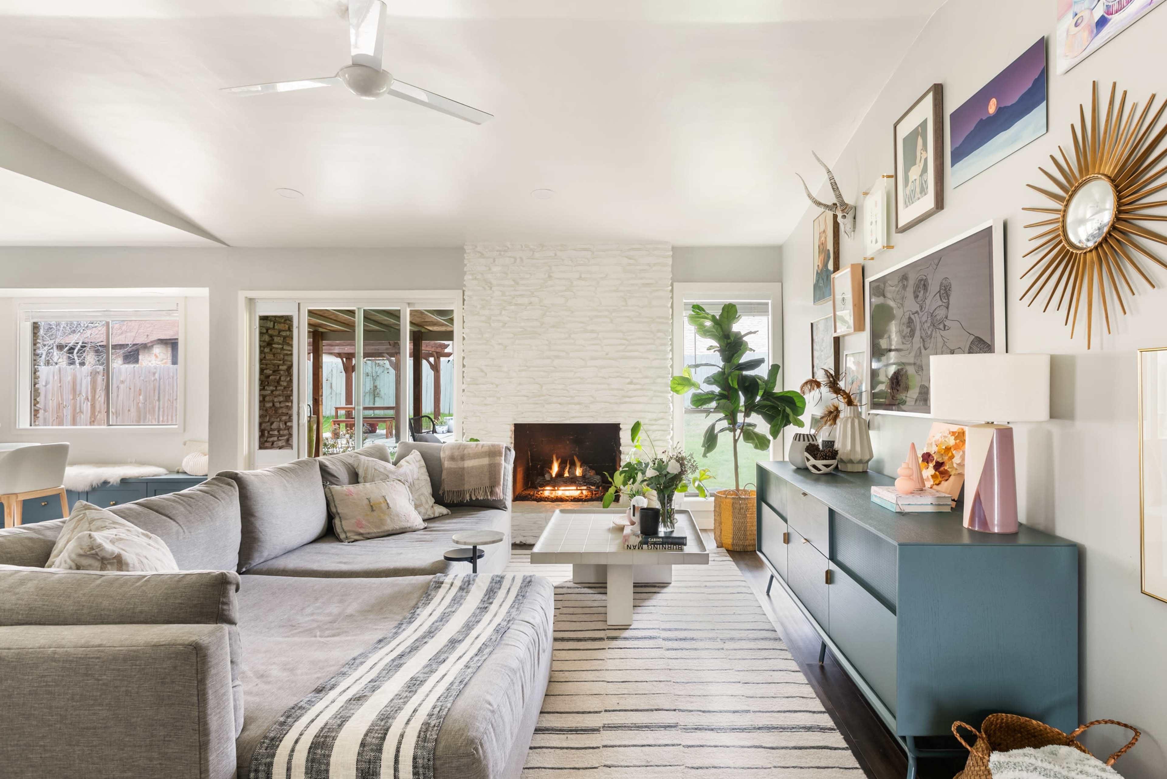 The living room features a sectional couch, a coffee table, a stone fireplace, and large windows that open to an outdoor space.