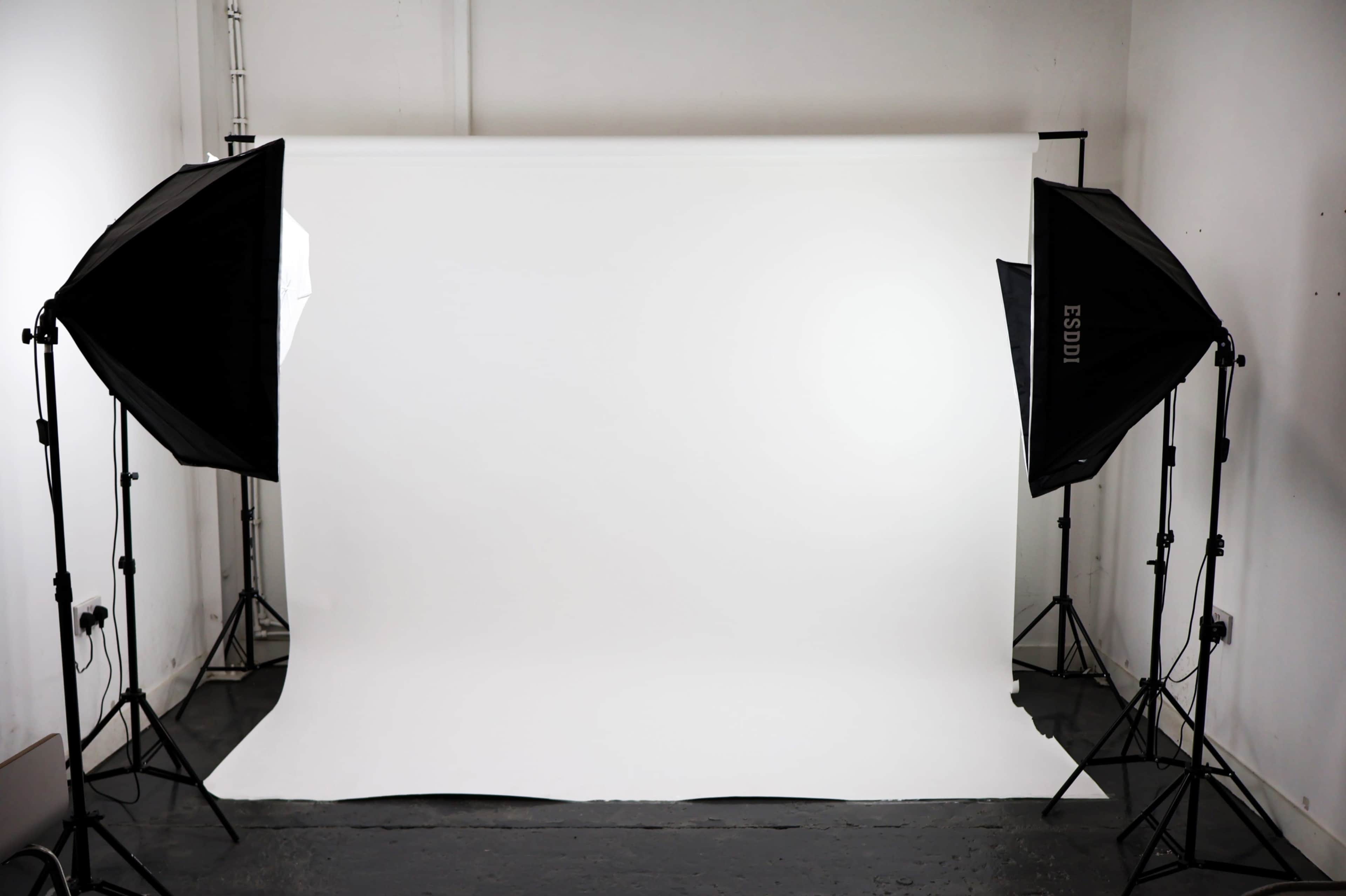 The image shows a photography studio setup with a white backdrop and two softbox lights positioned on either side.
