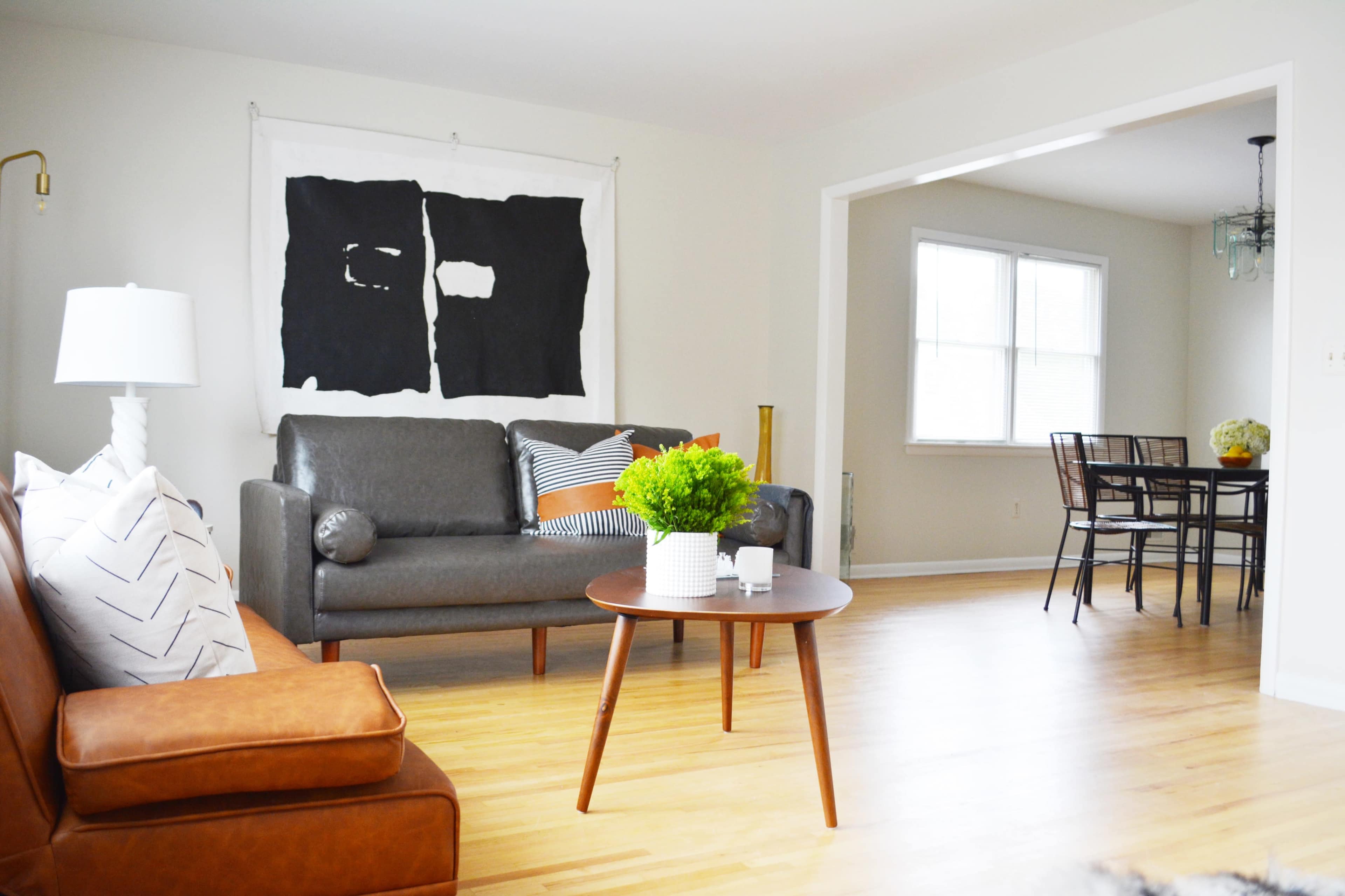 A living room with a gray sofa, a brown leather armchair, a round coffee table with a plant, and an adjacent dining area with a table and chairs.