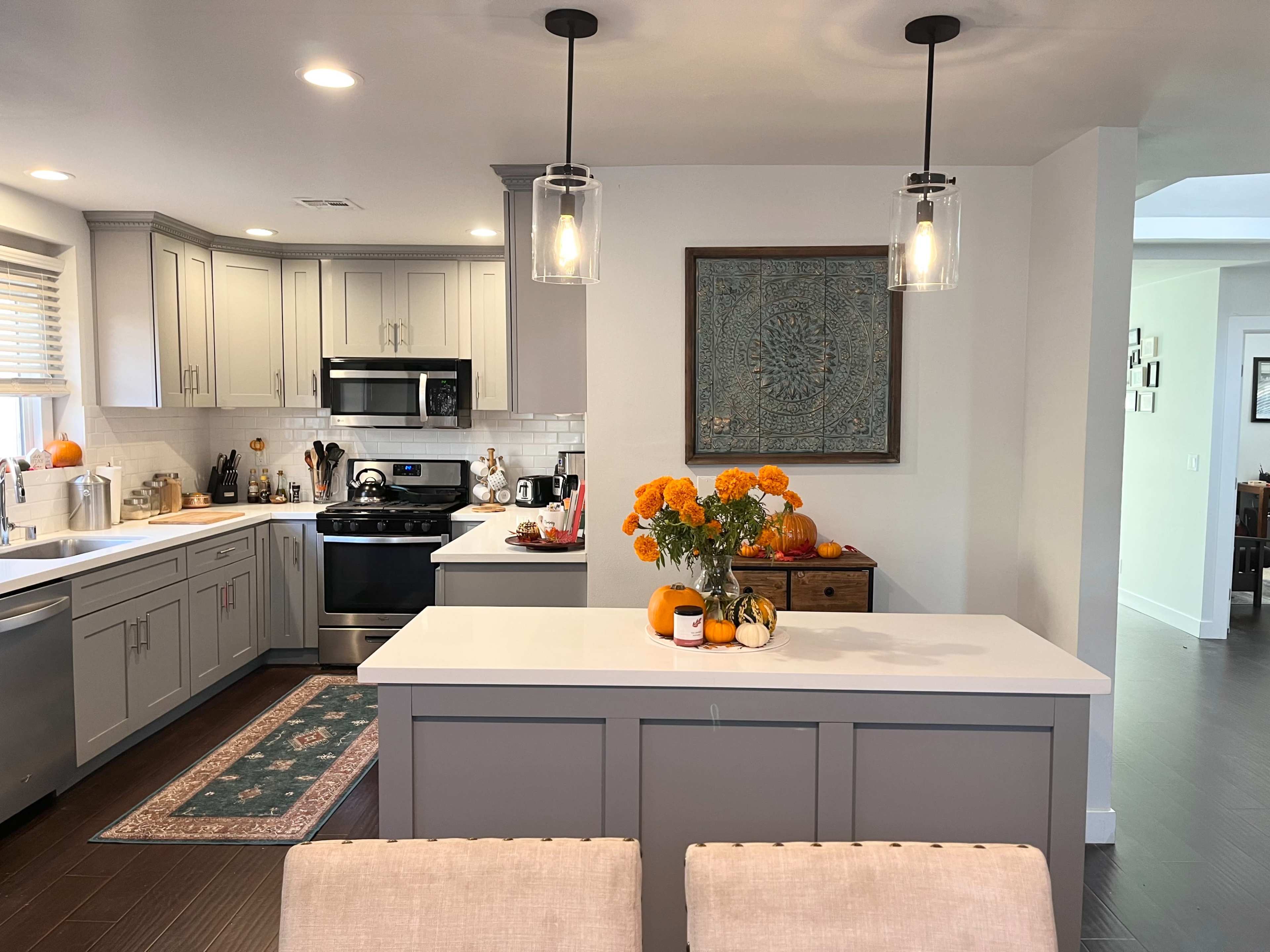 A modern kitchen with gray cabinets, a central island, and a vase of orange flowers on the counter.