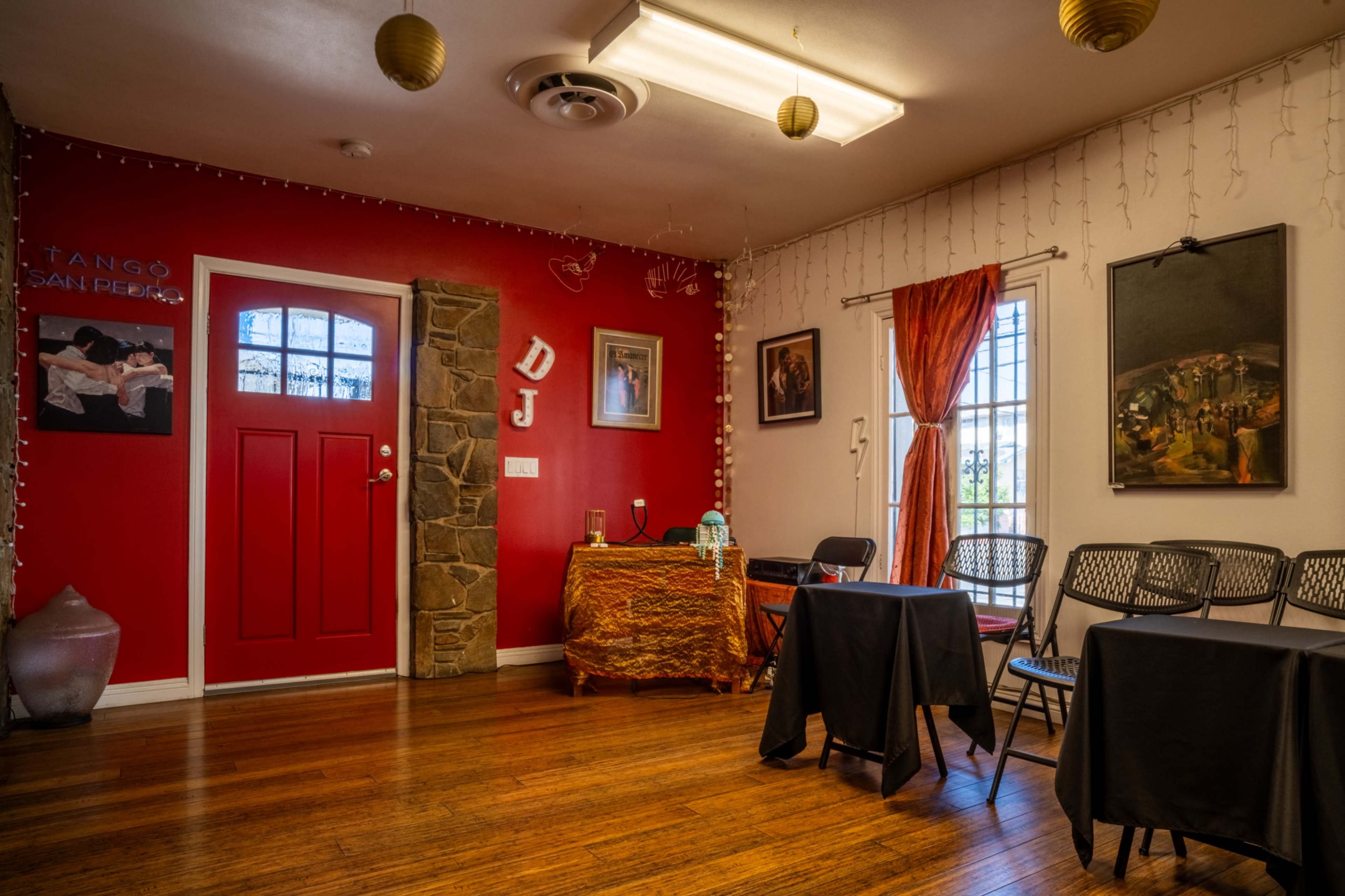 The image shows a colorful dance studio with red walls, a decorated entrance, several black tables, and string lights hanging from the ceiling.
