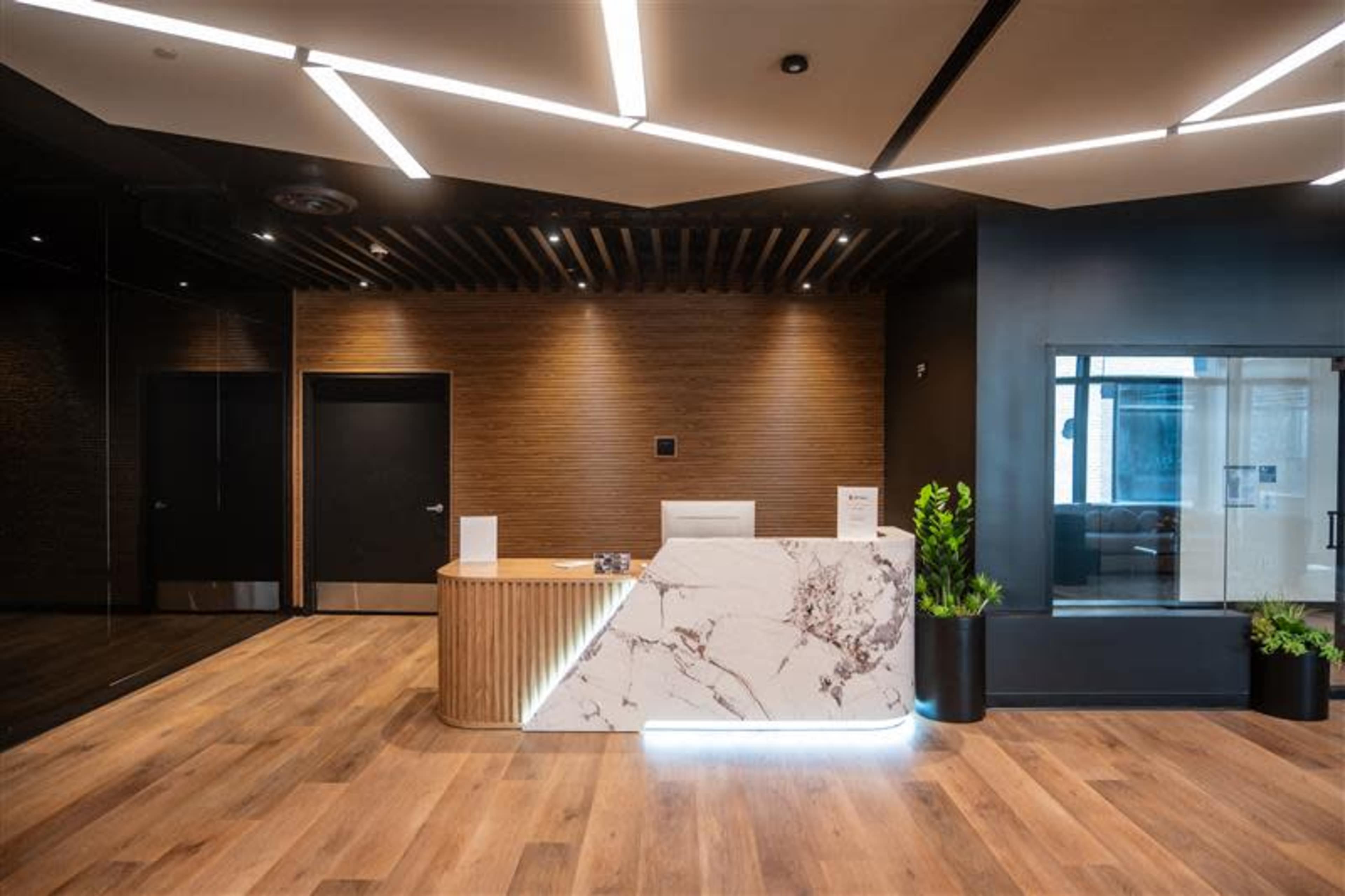 The image shows a modern reception area with a marble desk, wooden paneling, and sleek lighting.