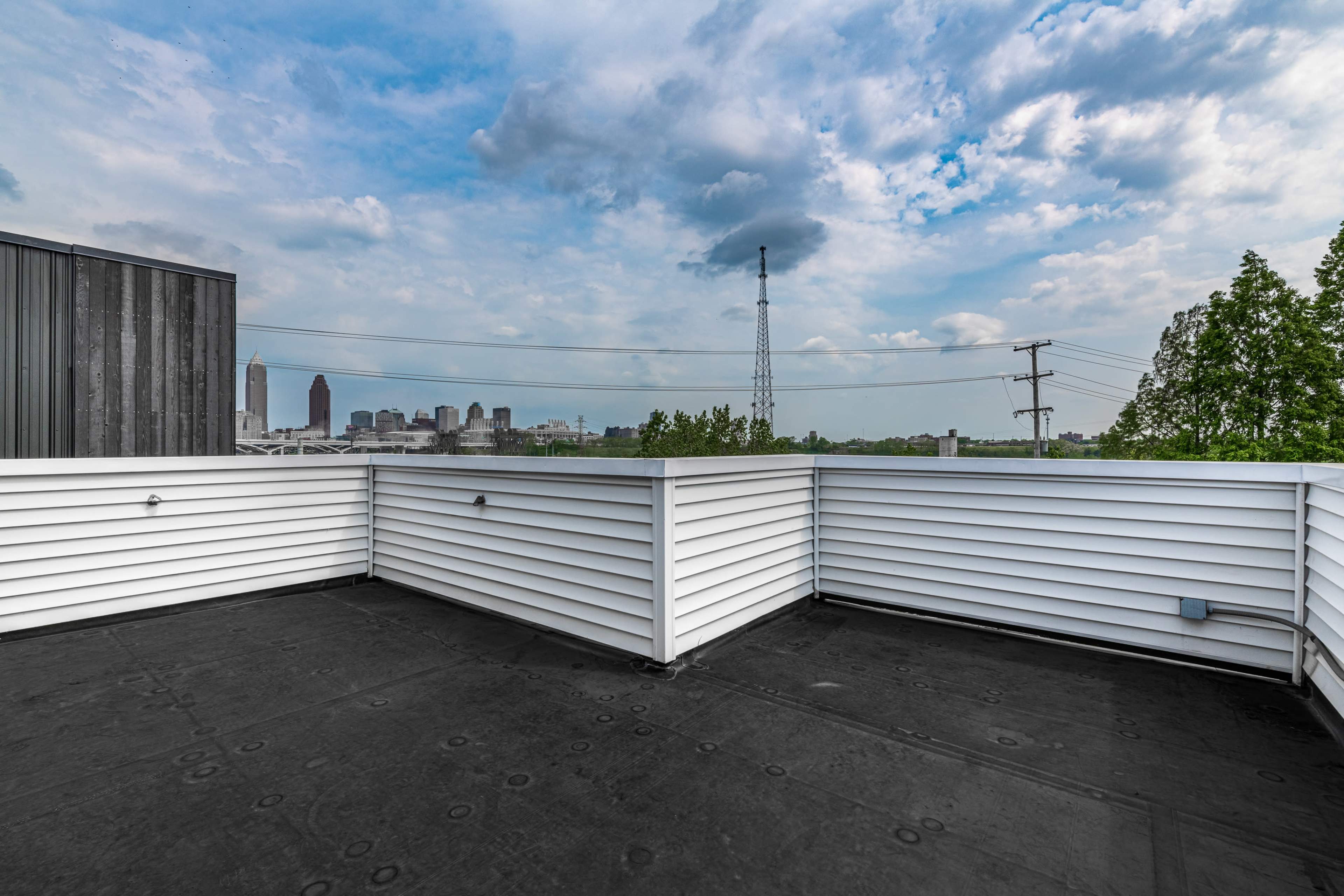 A rooftop terrace with white railings overlooking a city skyline under a partly cloudy sky.