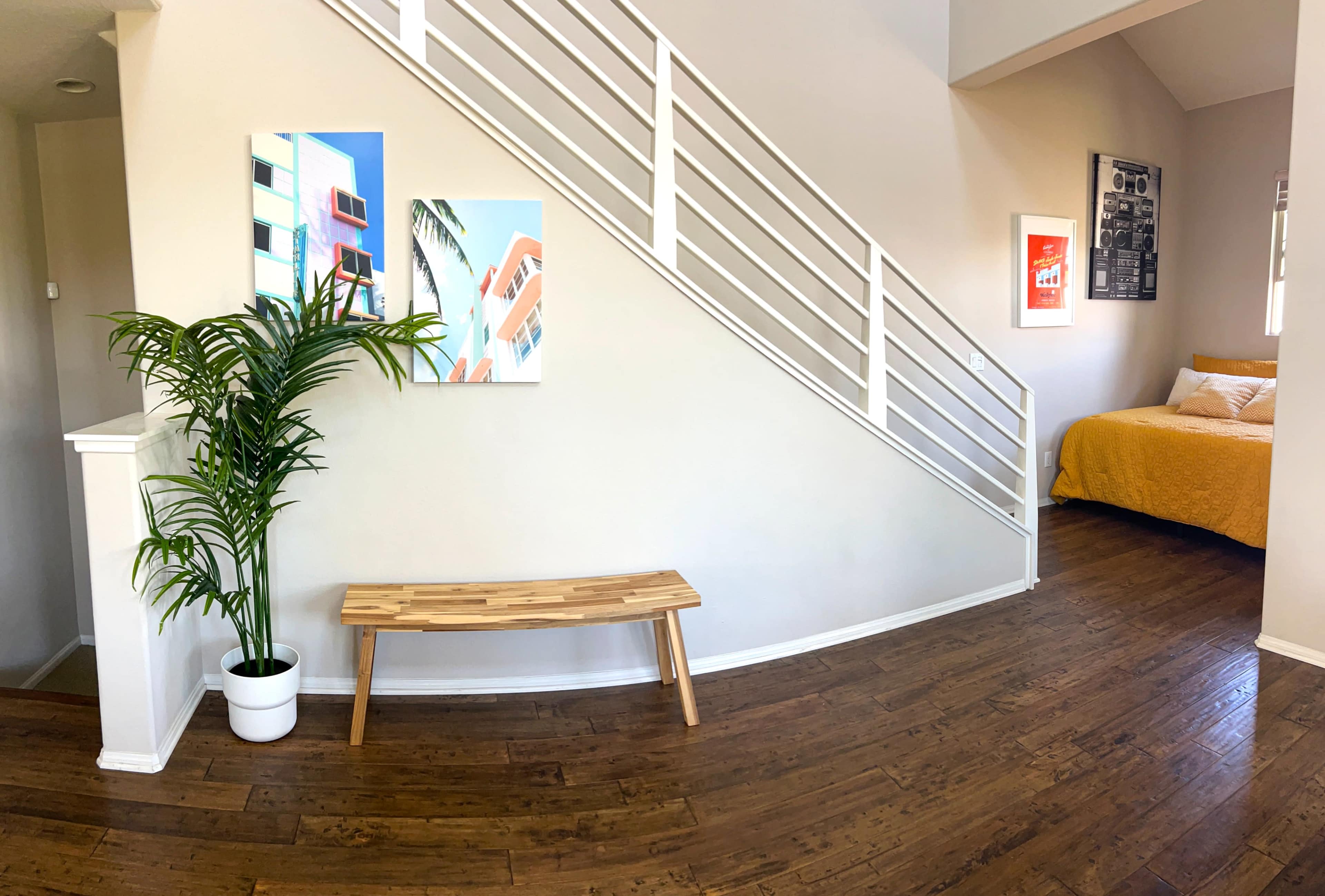 A modern entryway featuring a wooden bench, potted plant, and a staircase leading to an upper level, with colorful wall art displayed nearby.