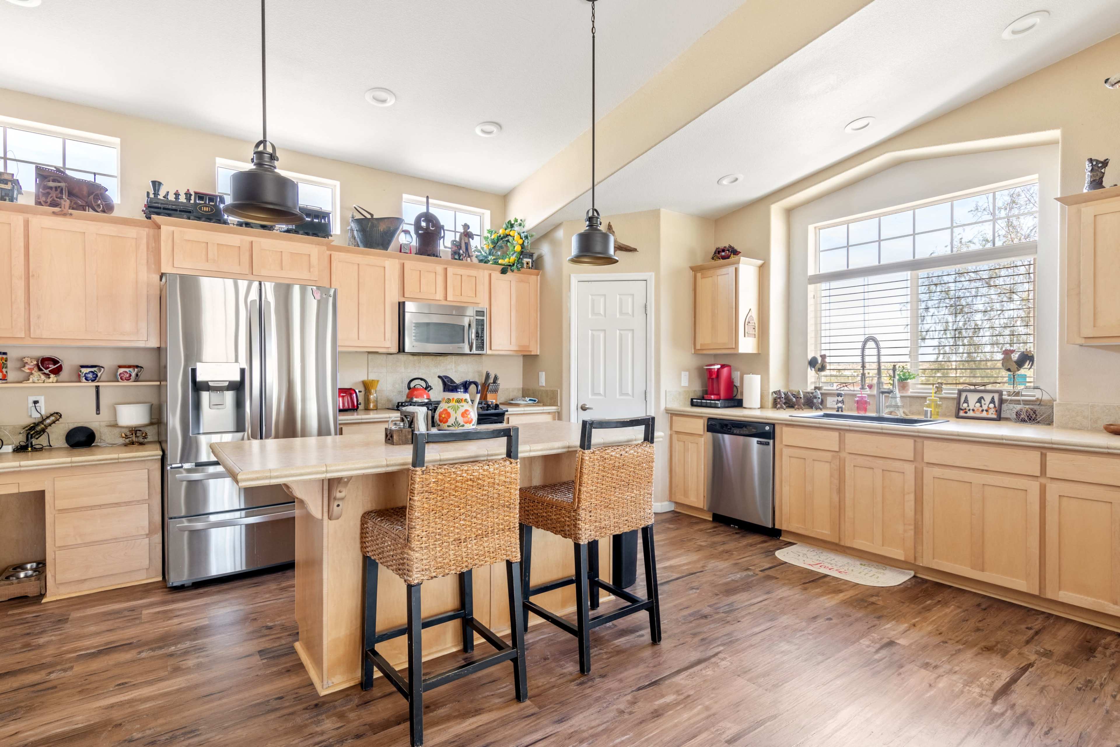 A modern kitchen features wooden cabinetry, stainless steel appliances, and a central island with two bar stools.