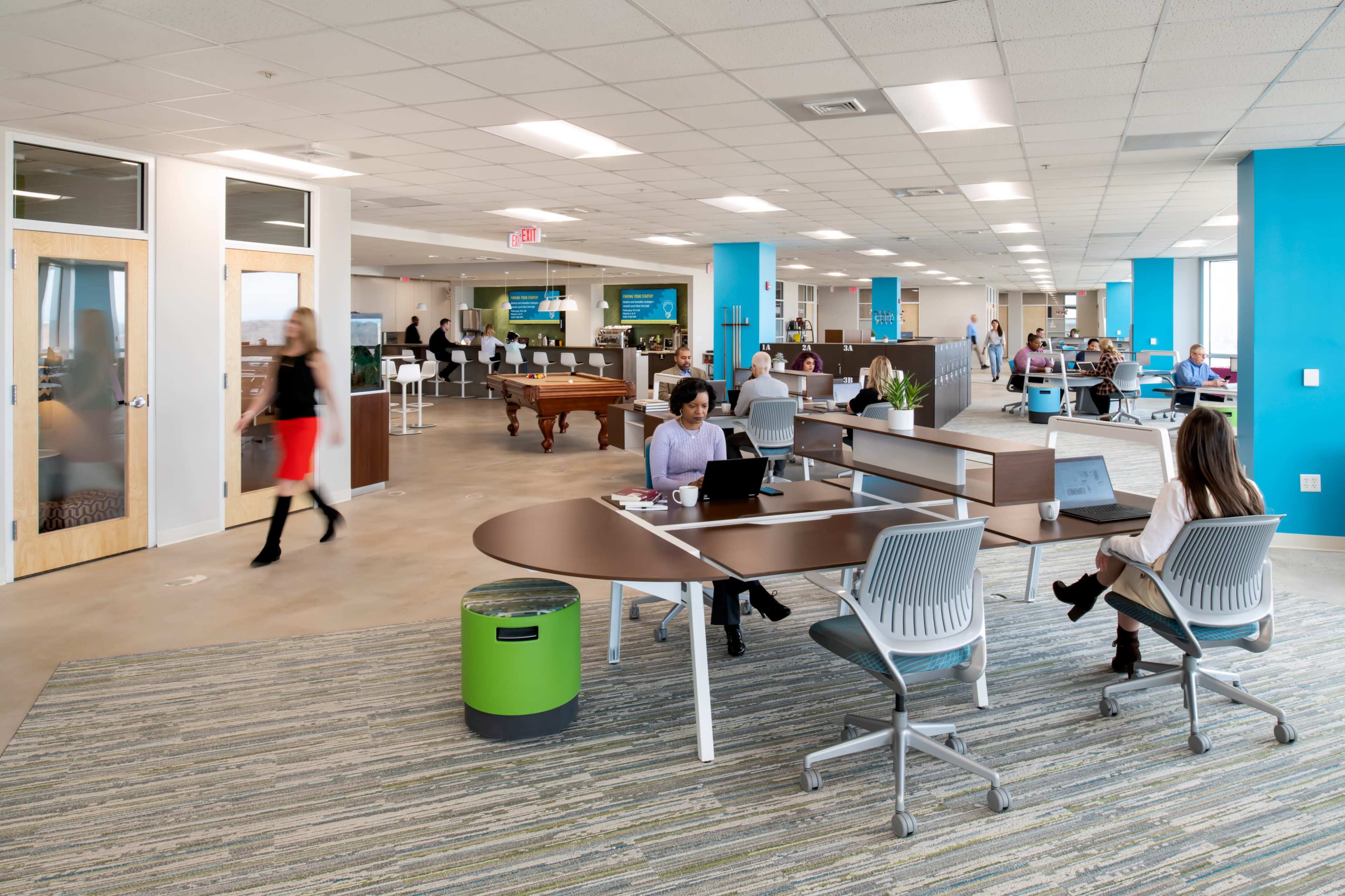 A modern office space with multiple workstations, a pool table, and employees engaged in various activities.
