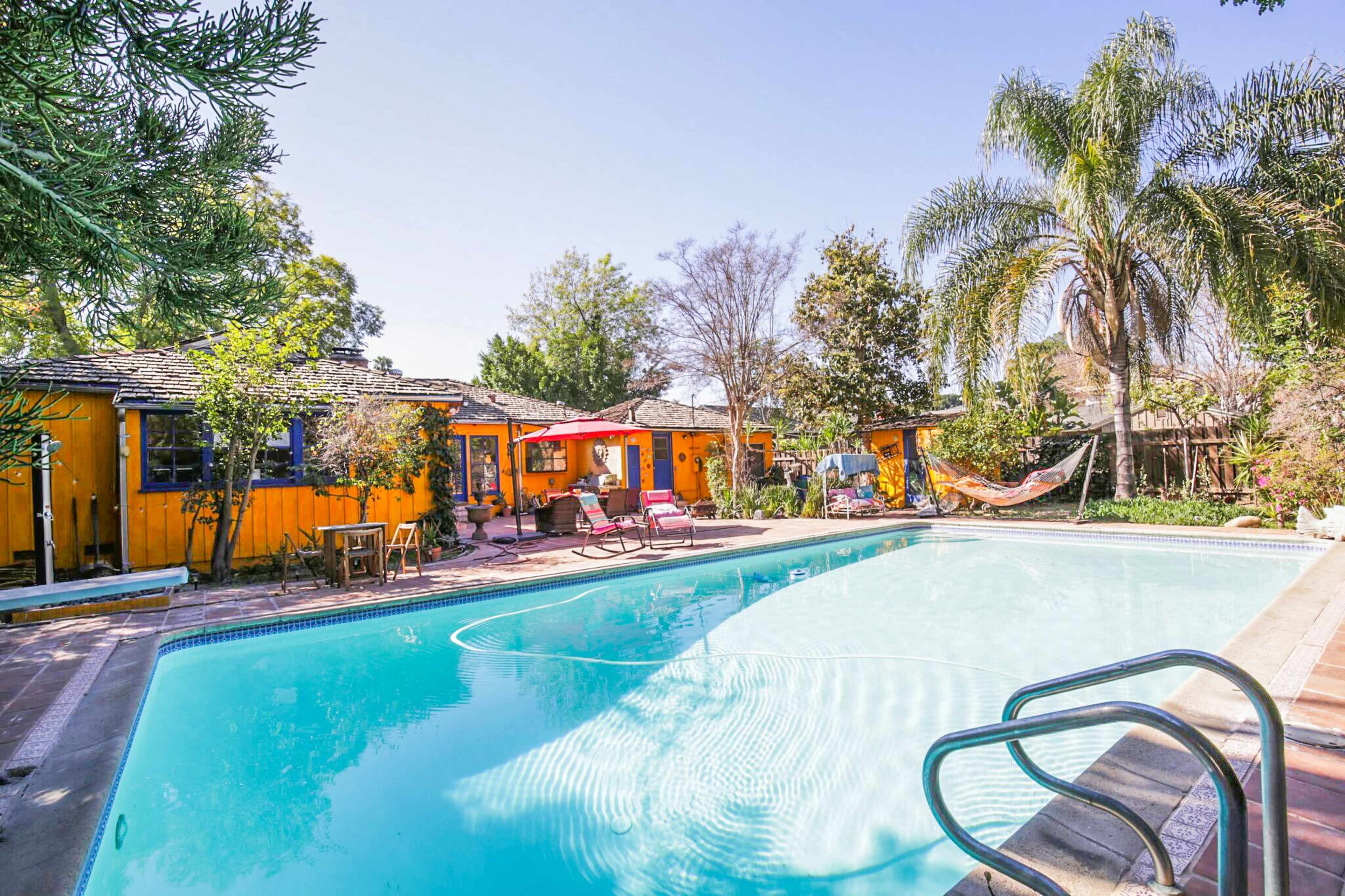 A swimming pool surrounded by colorful cottages, lounge chairs, and palm trees.
