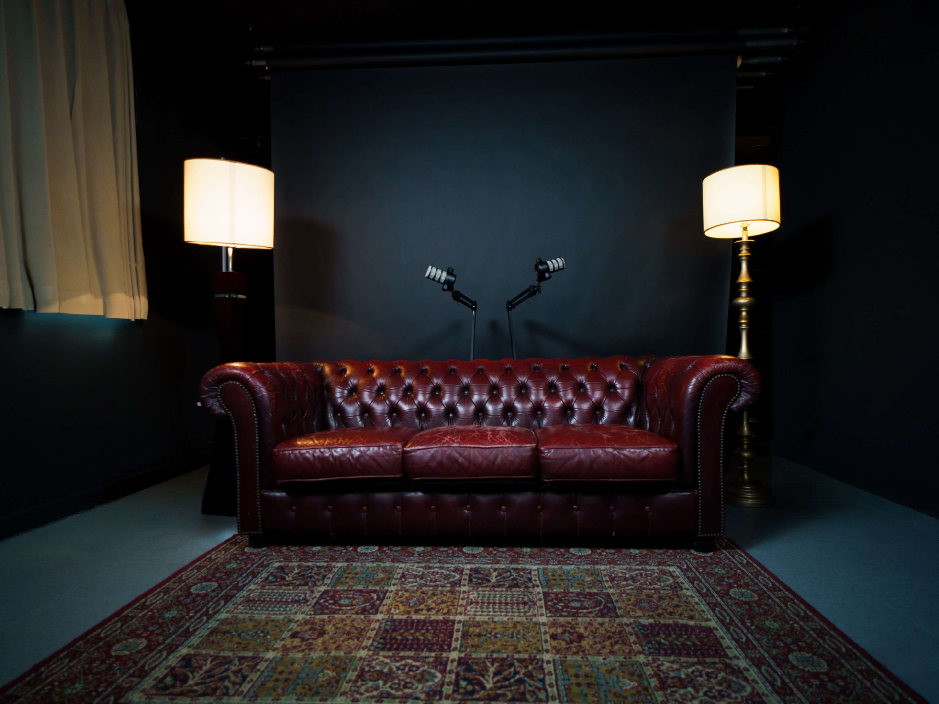 The image features a deep red leather couch in a dimly lit room, flanked by two standing lamps and a patterned rug.