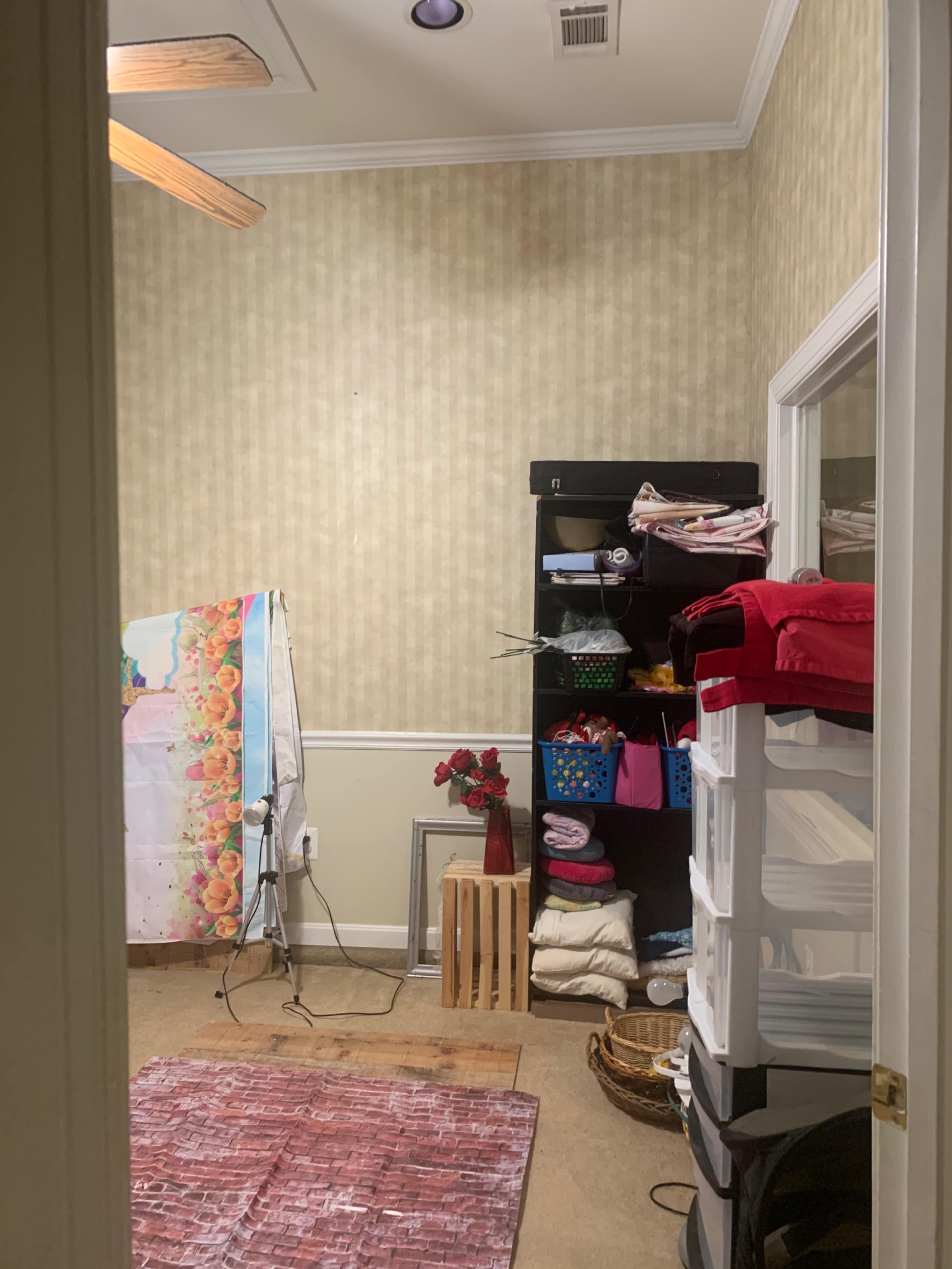 A small room with a bookshelf filled with colorful storage bins, a hanging sheet, and various fabric items arranged on a rack.