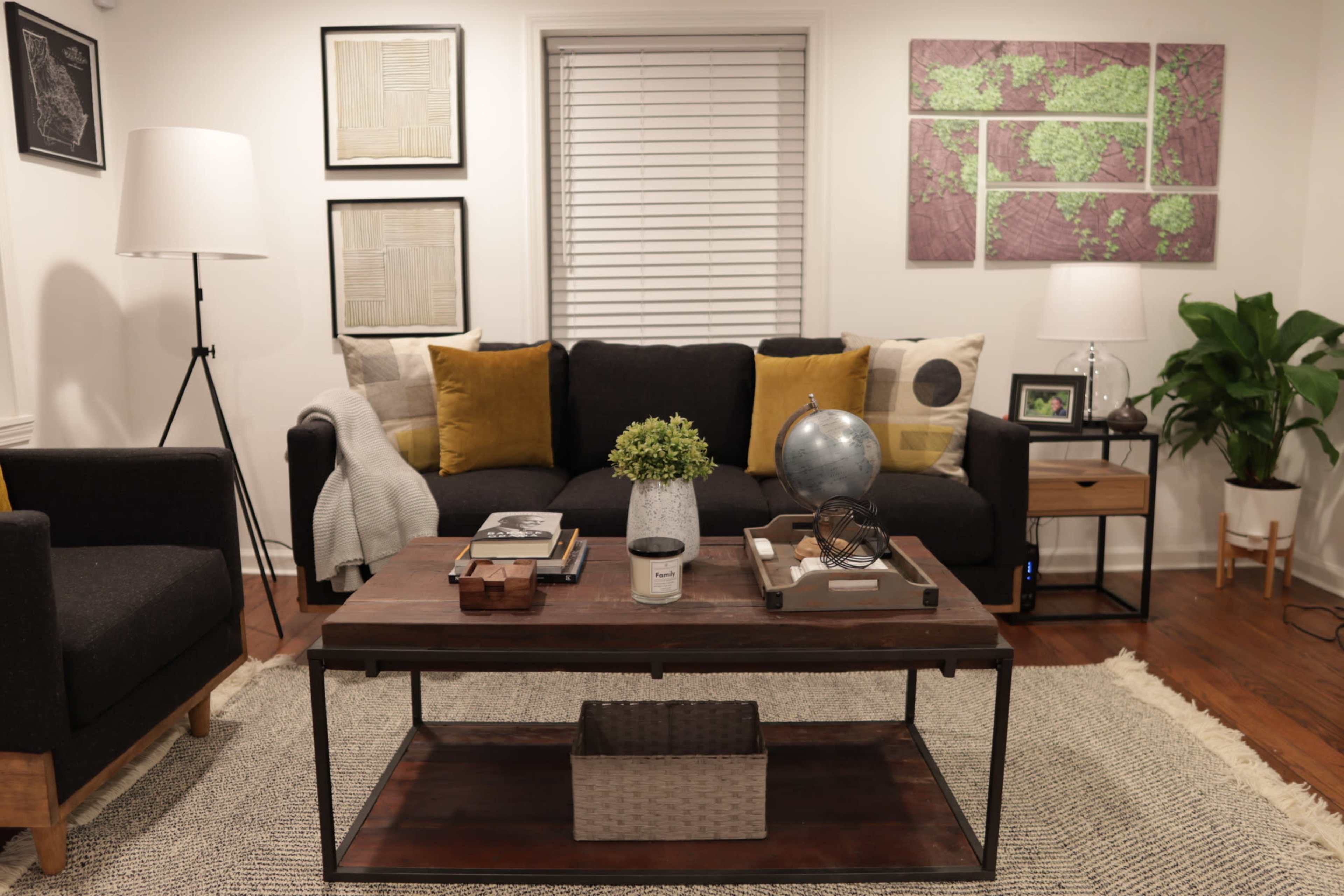 A modern living room features a black sofa with yellow pillows, a wooden coffee table with decorative items, and framed artwork on the walls.