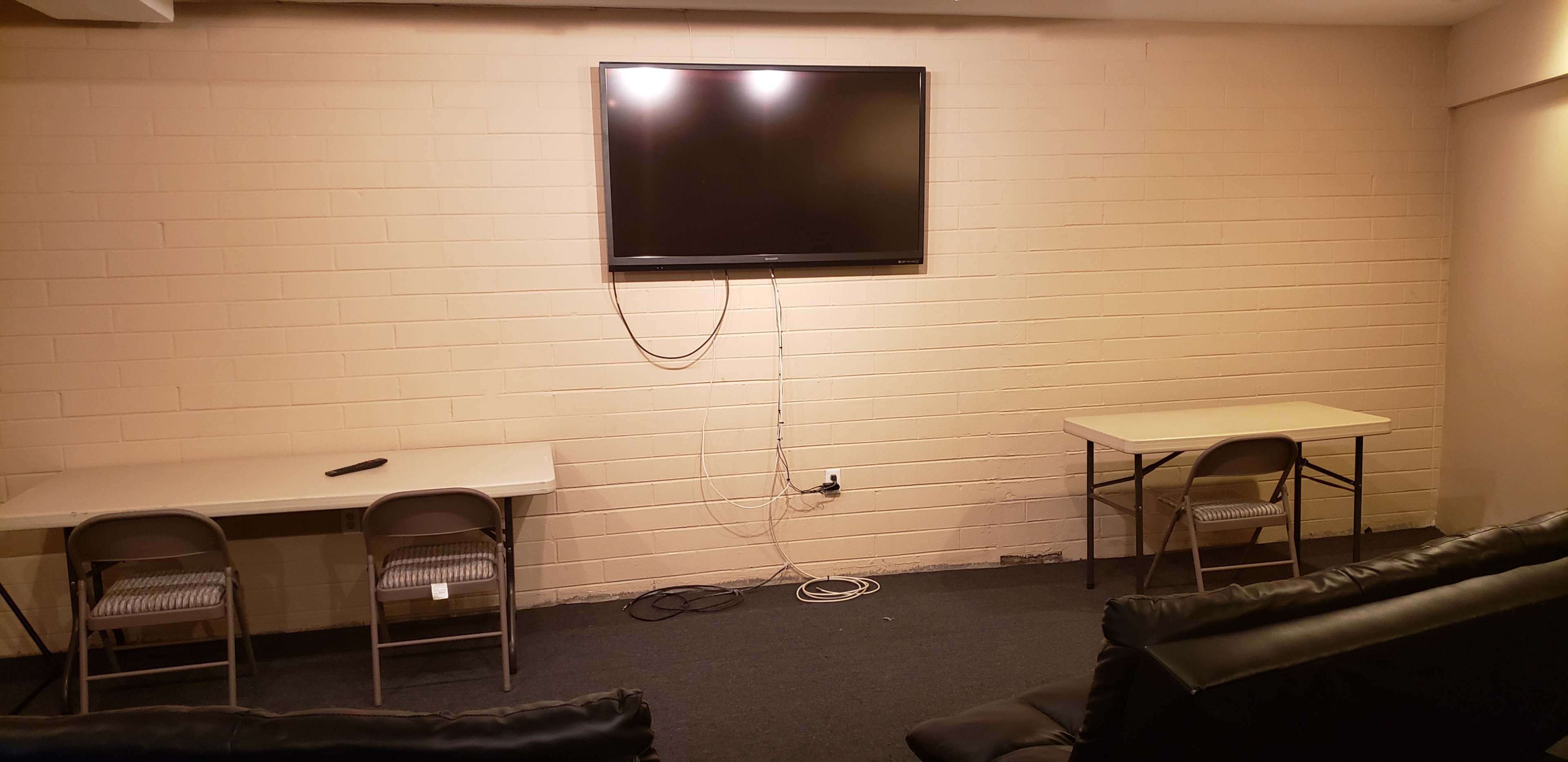 A sparsely furnished room features two tables, chairs, and a wall-mounted television.