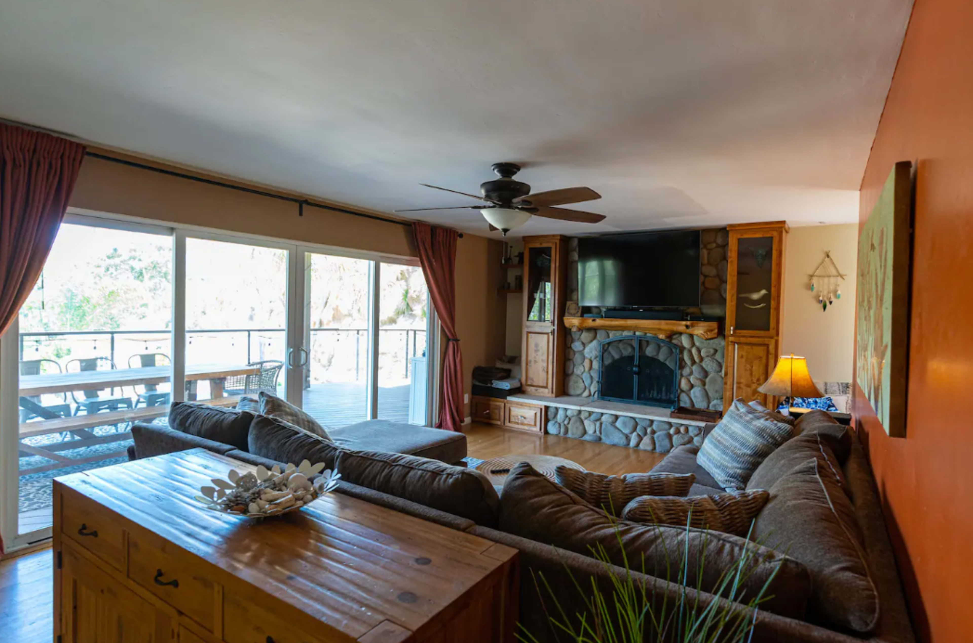 The living room features a large sectional sofa, a stone fireplace, a mounted television, and sliding glass doors leading to a deck.