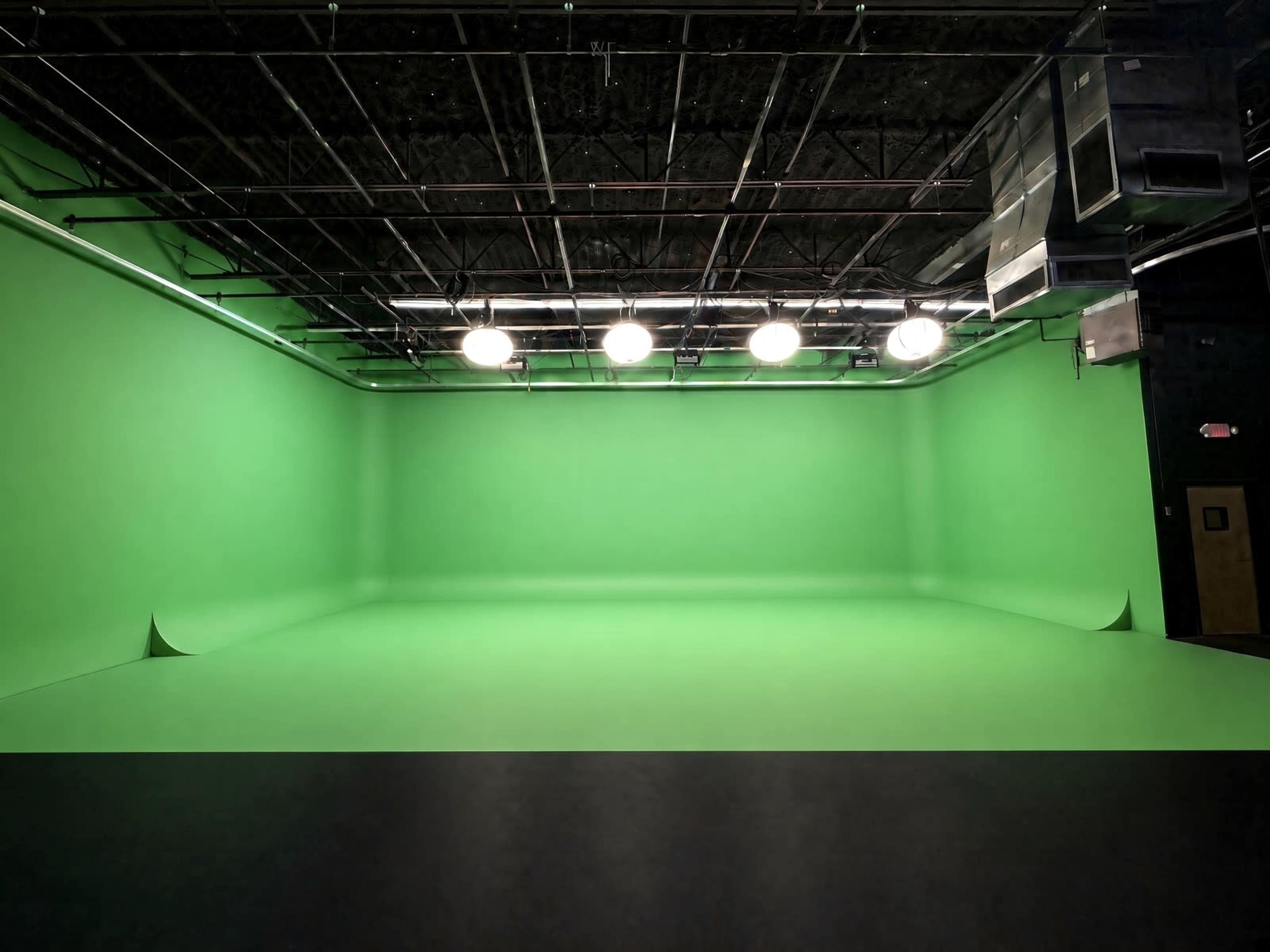 The image shows a large green screen studio with bright overhead lights and a seamless green backdrop.