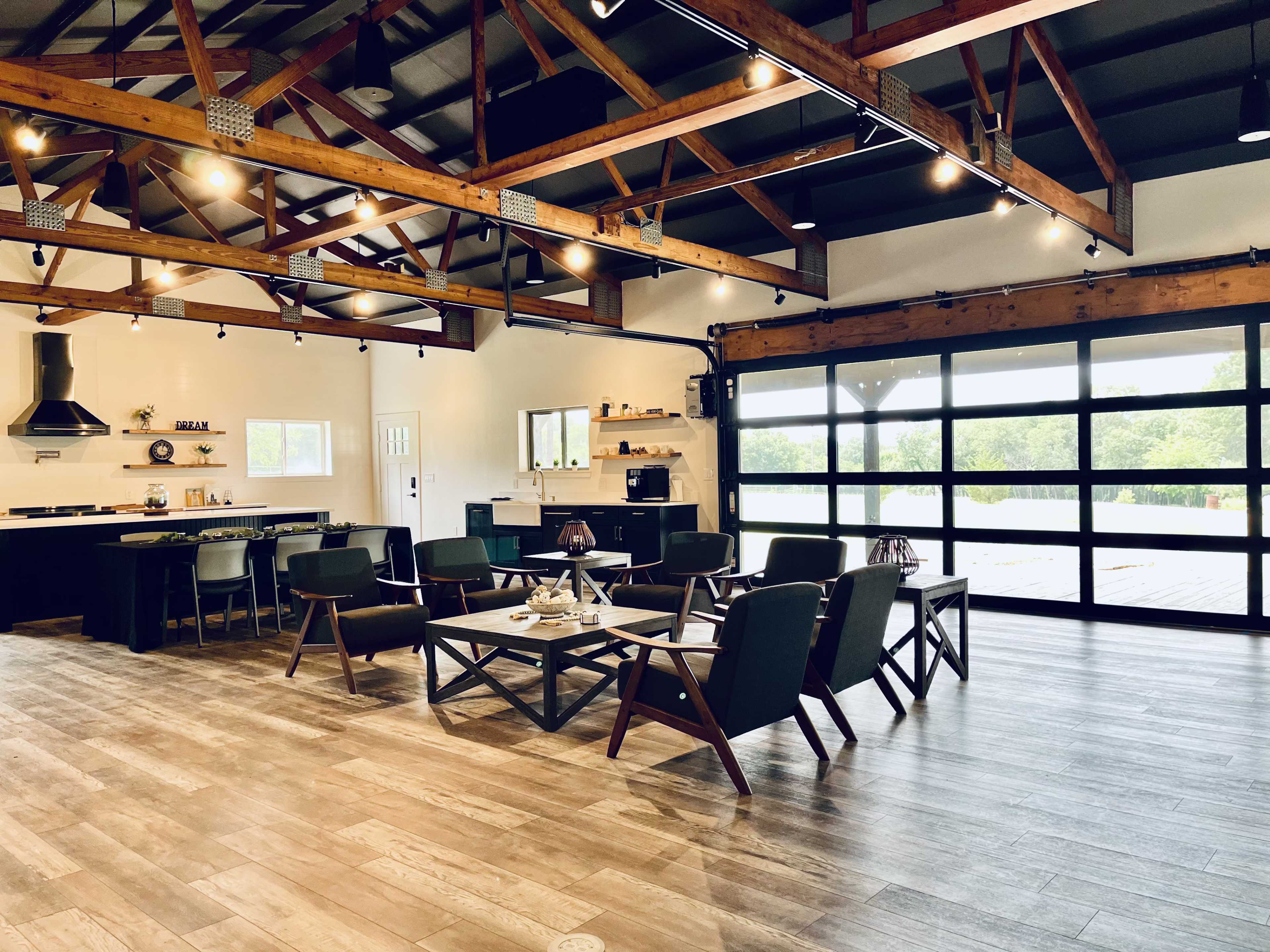 A spacious, modern interior with exposed wooden beams, a kitchen area, and seating arrangements around a central coffee table.