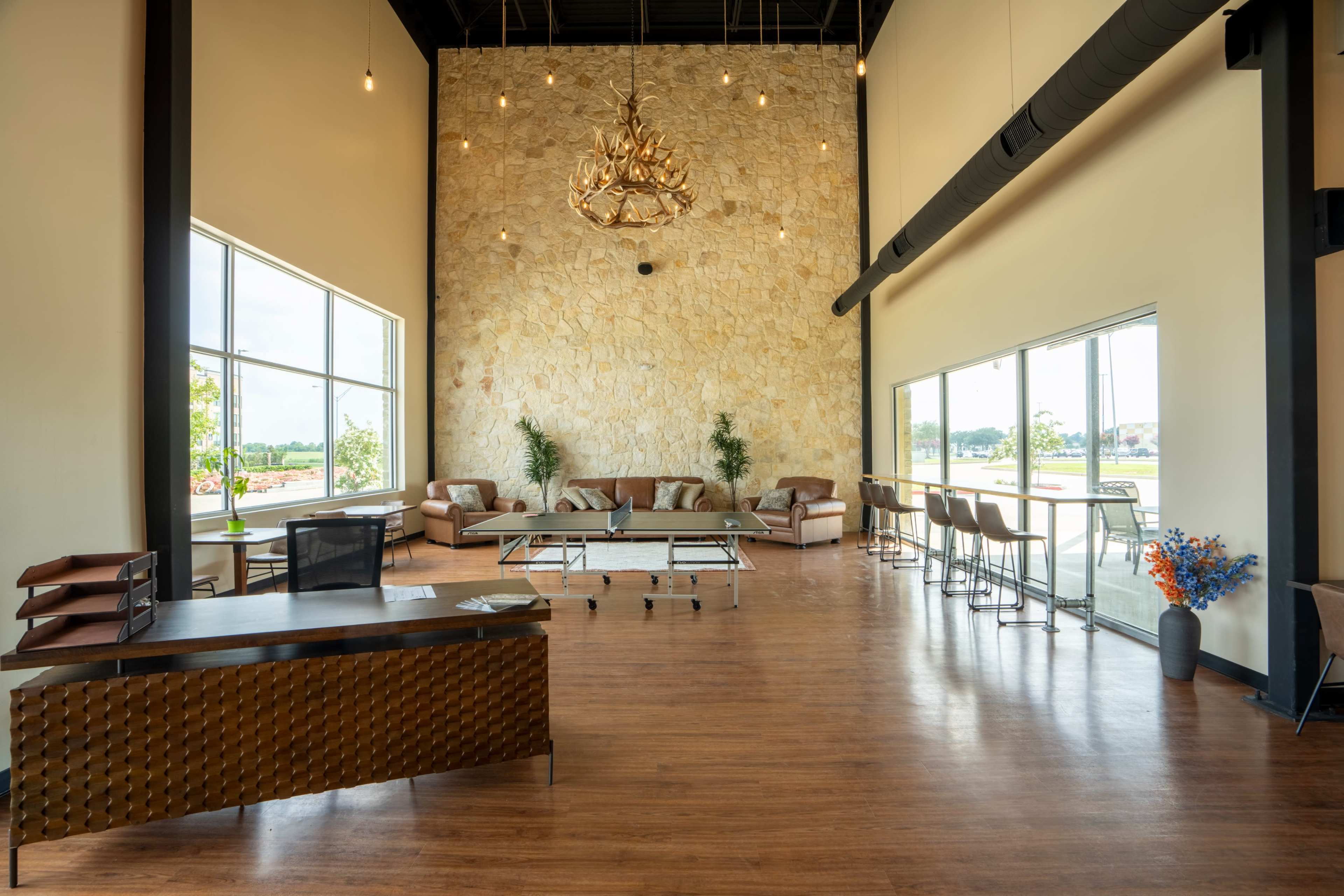 A modern, spacious interior with a stone accent wall, large windows, and a reception area featuring a desk and seating arrangements.