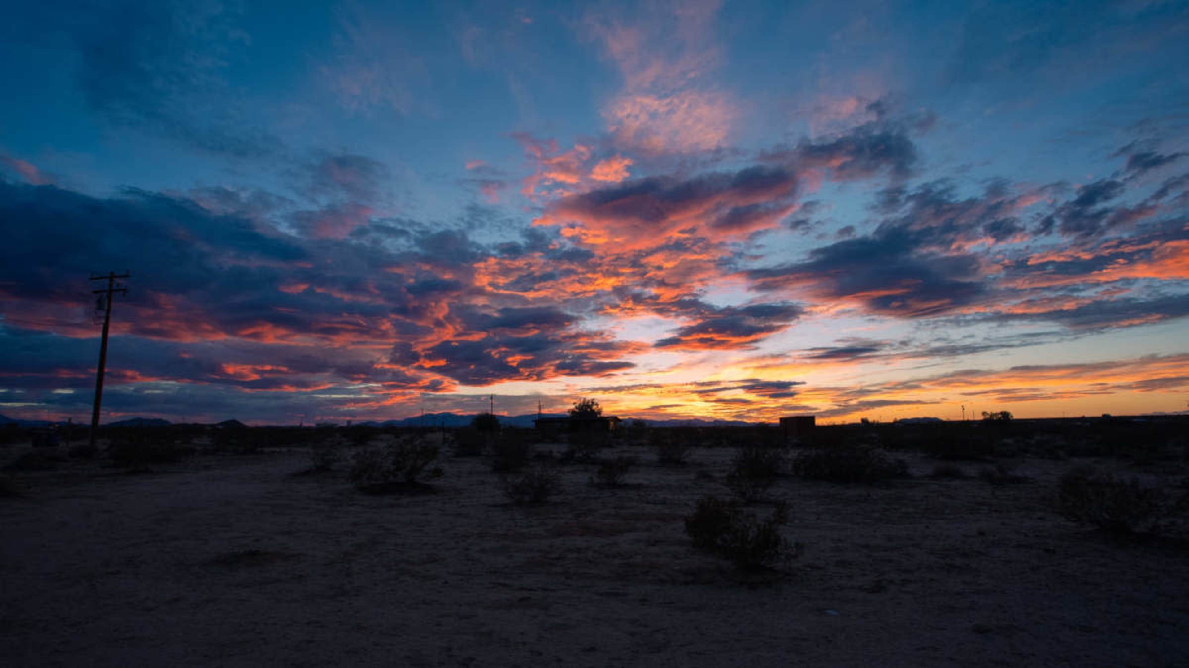 The image shows a desert landscape at sunset, featuring a vibrant sky filled with colorful clouds.