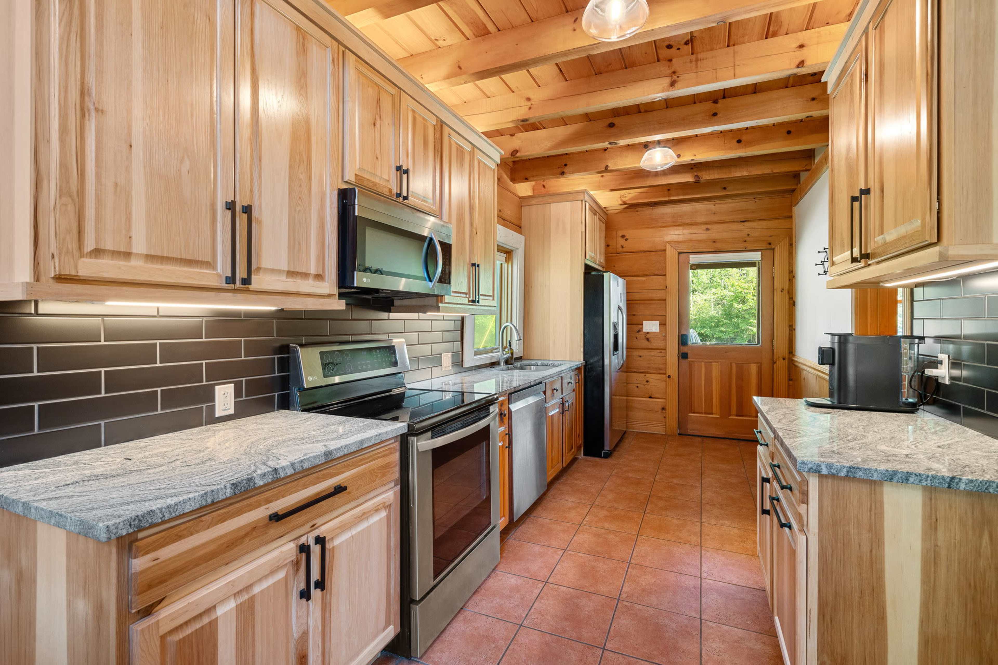 A kitchen features wooden cabinets, granite countertops, stainless steel appliances, and a tile backsplash, with natural light coming from a nearby window.