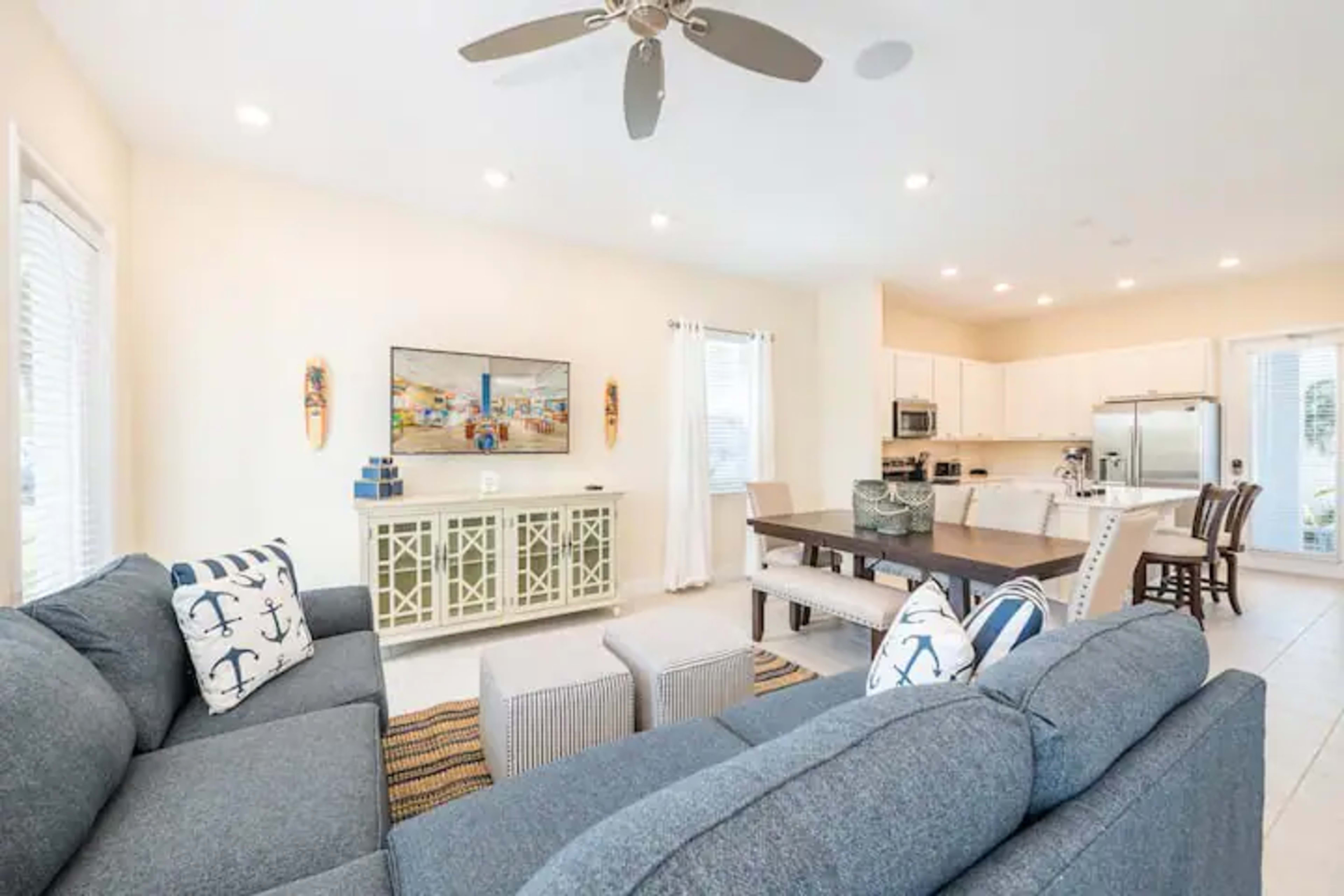 A living room with a sectional sofa, a television on the wall, and a dining area connected to a kitchen with modern appliances.