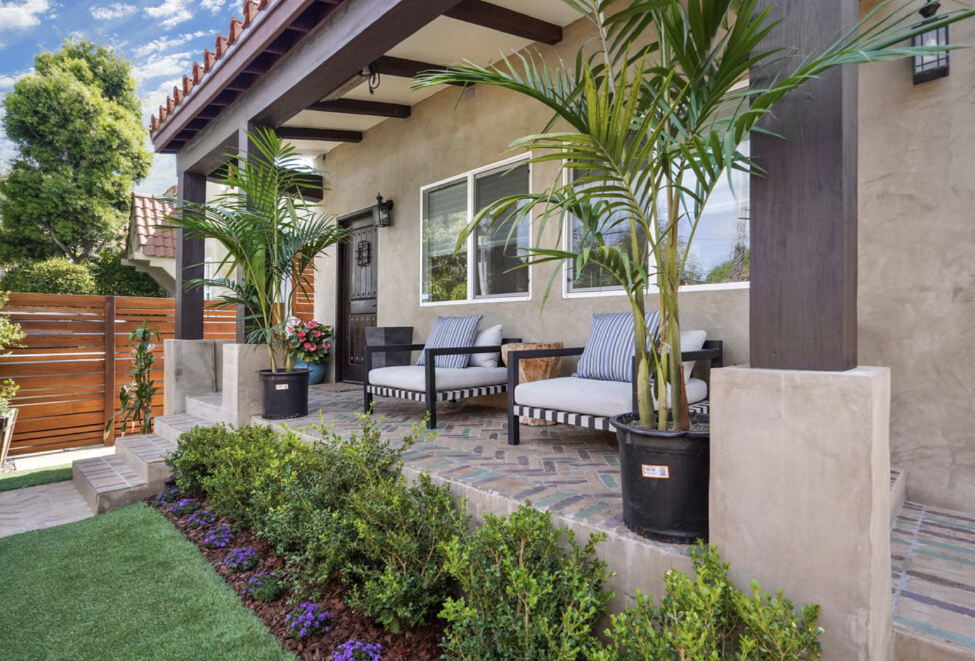 A front porch of a house with two chairs, potted plants, and a landscaped area.
