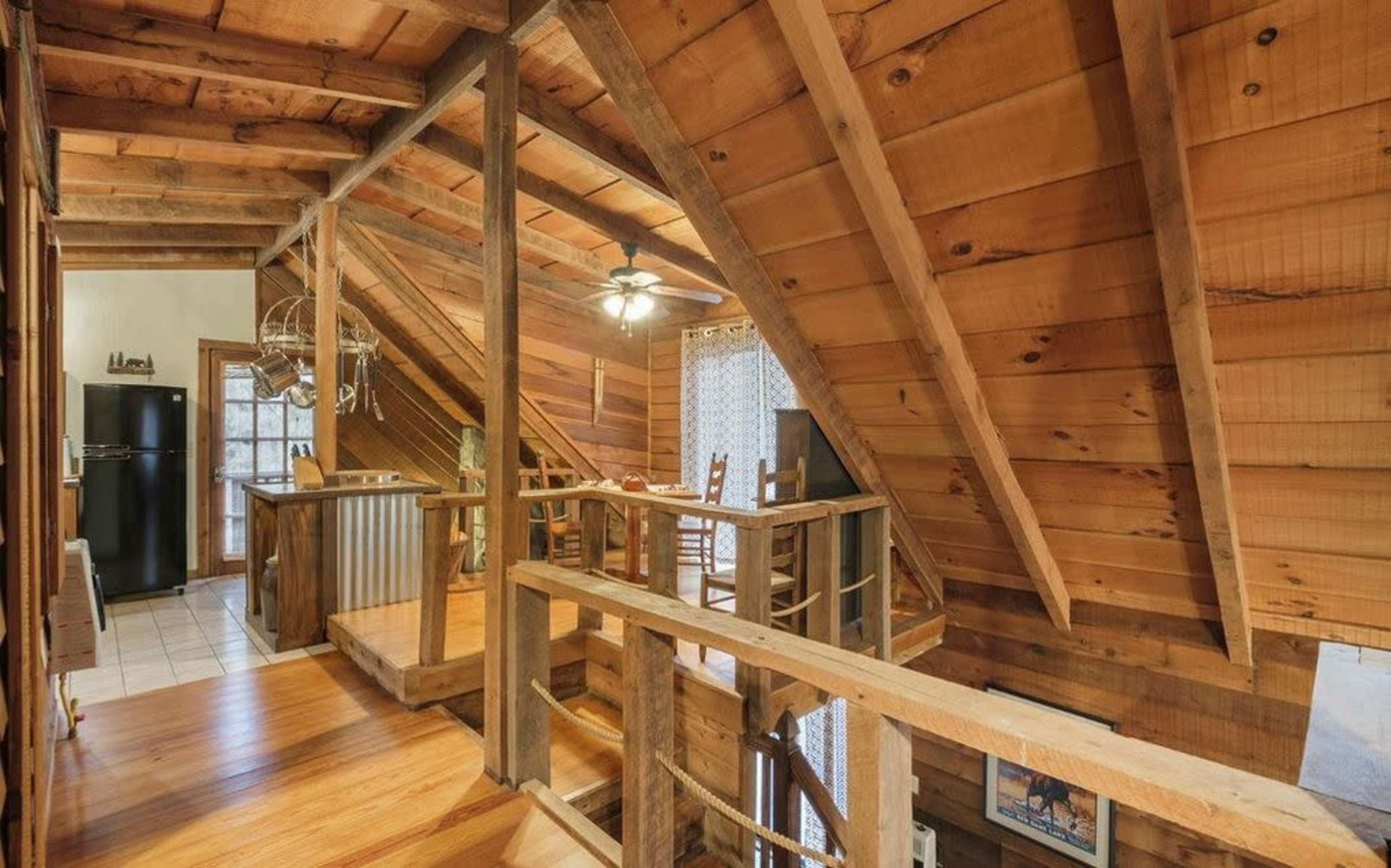 An interior view of a wooden lodge with sloped ceilings, an open loft area, and a kitchen on one side.