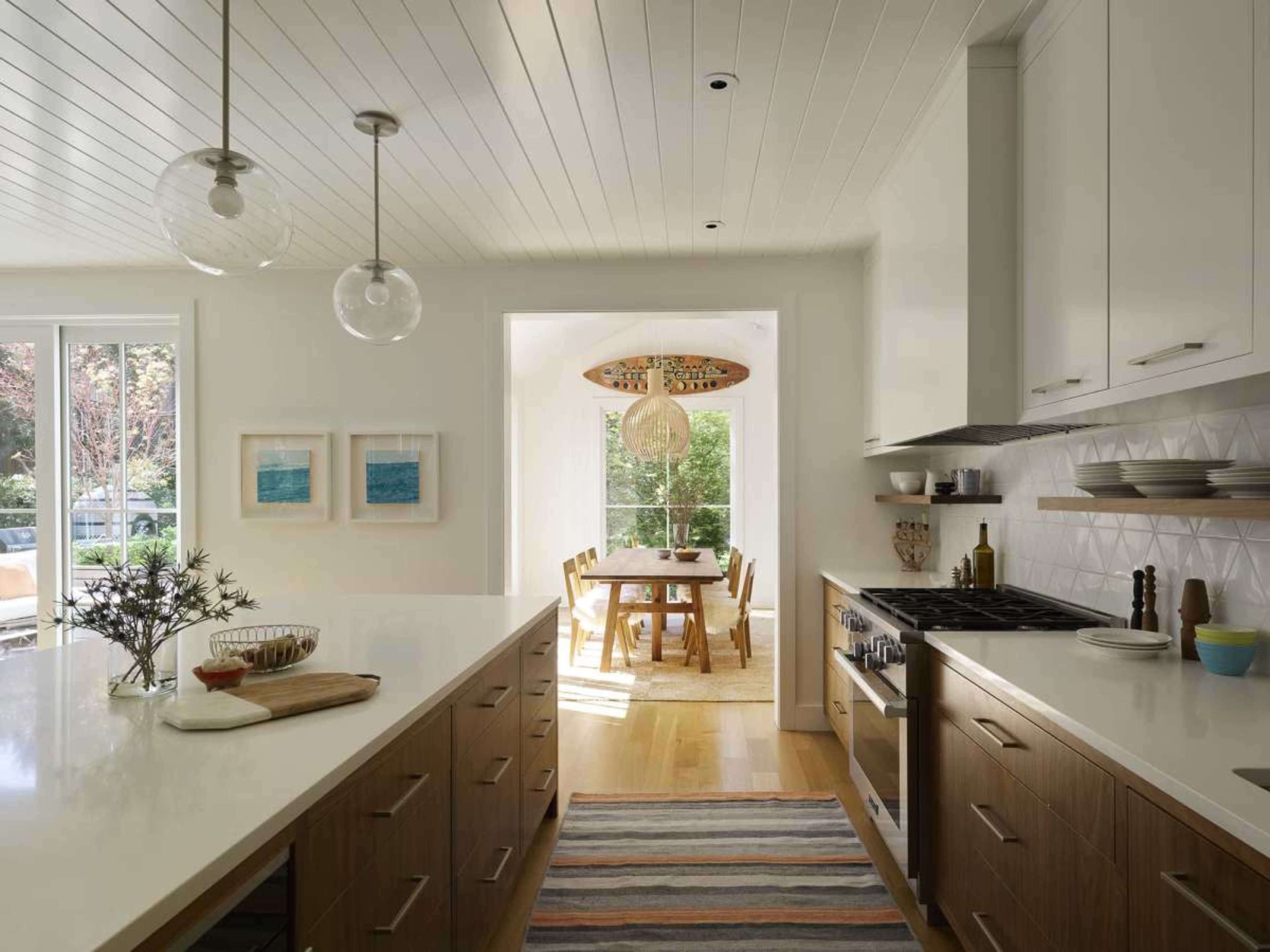 A modern kitchen features an island with a countertop, cabinetry, and a view into a dining area illuminated by natural light.