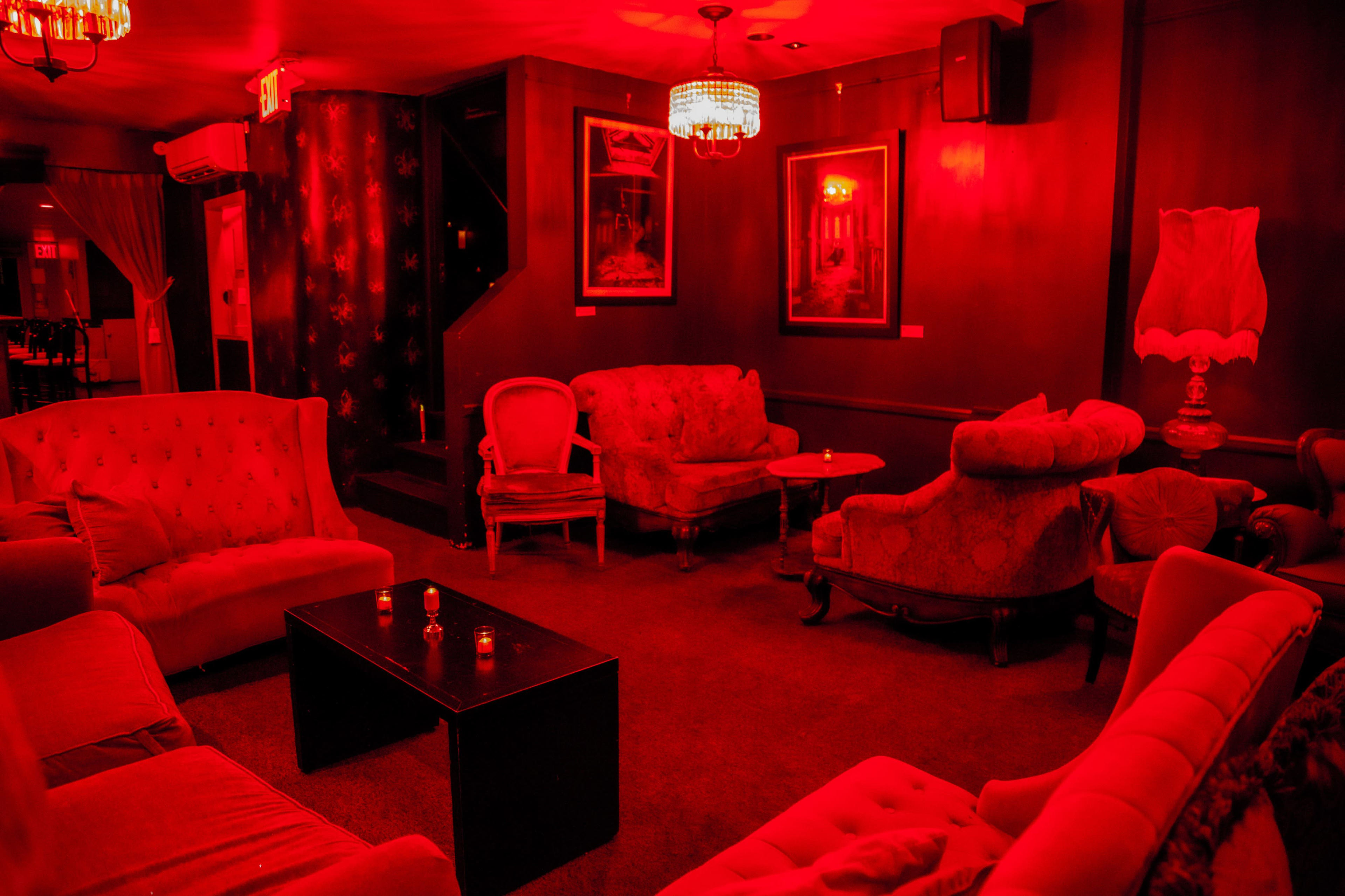 A lounge area with red walls and lighting, featuring several vintage-style sofas and a central table.