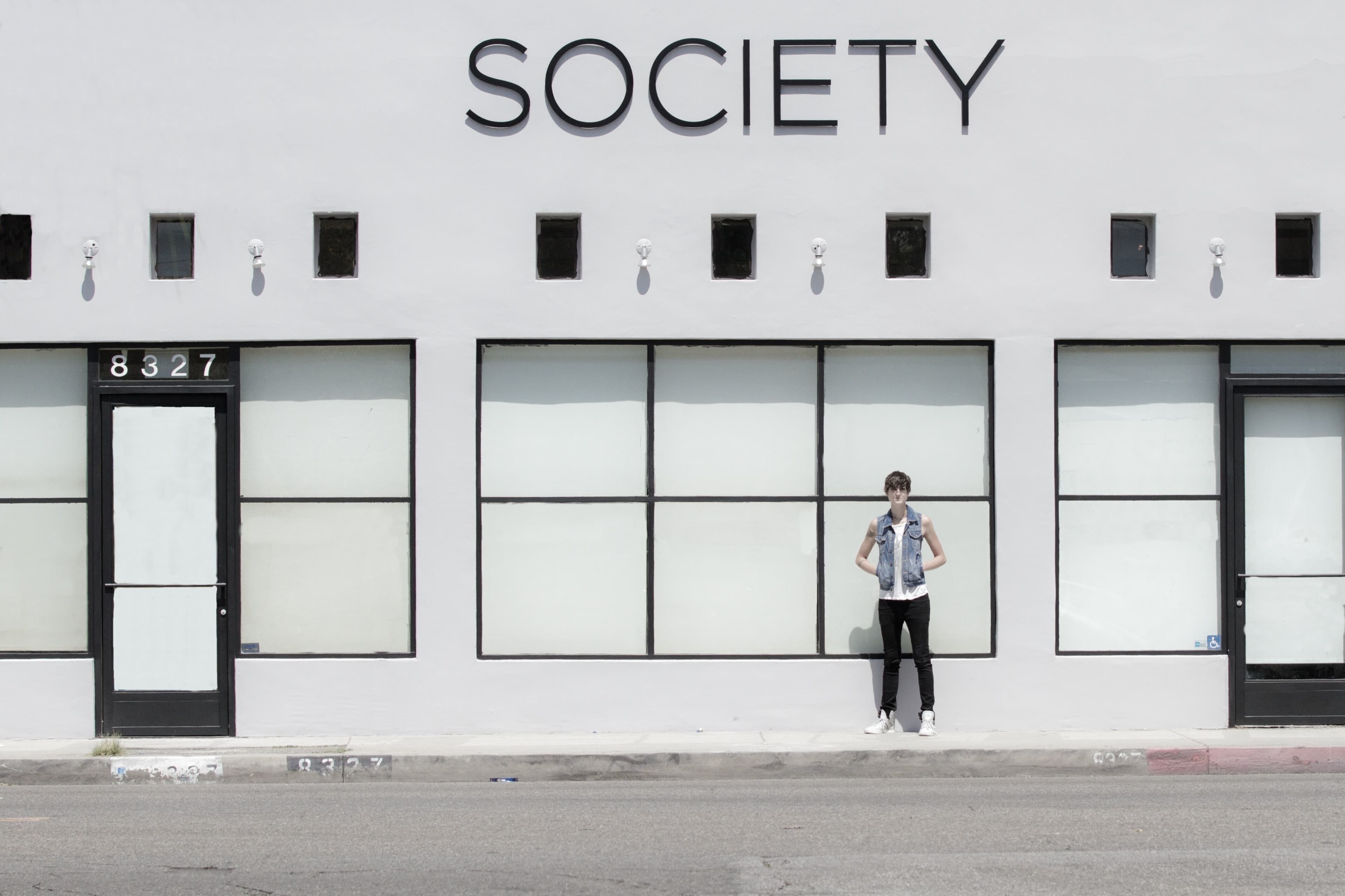 A person stands in front of a building with the word "SOCIETY" prominently displayed above large windows.
