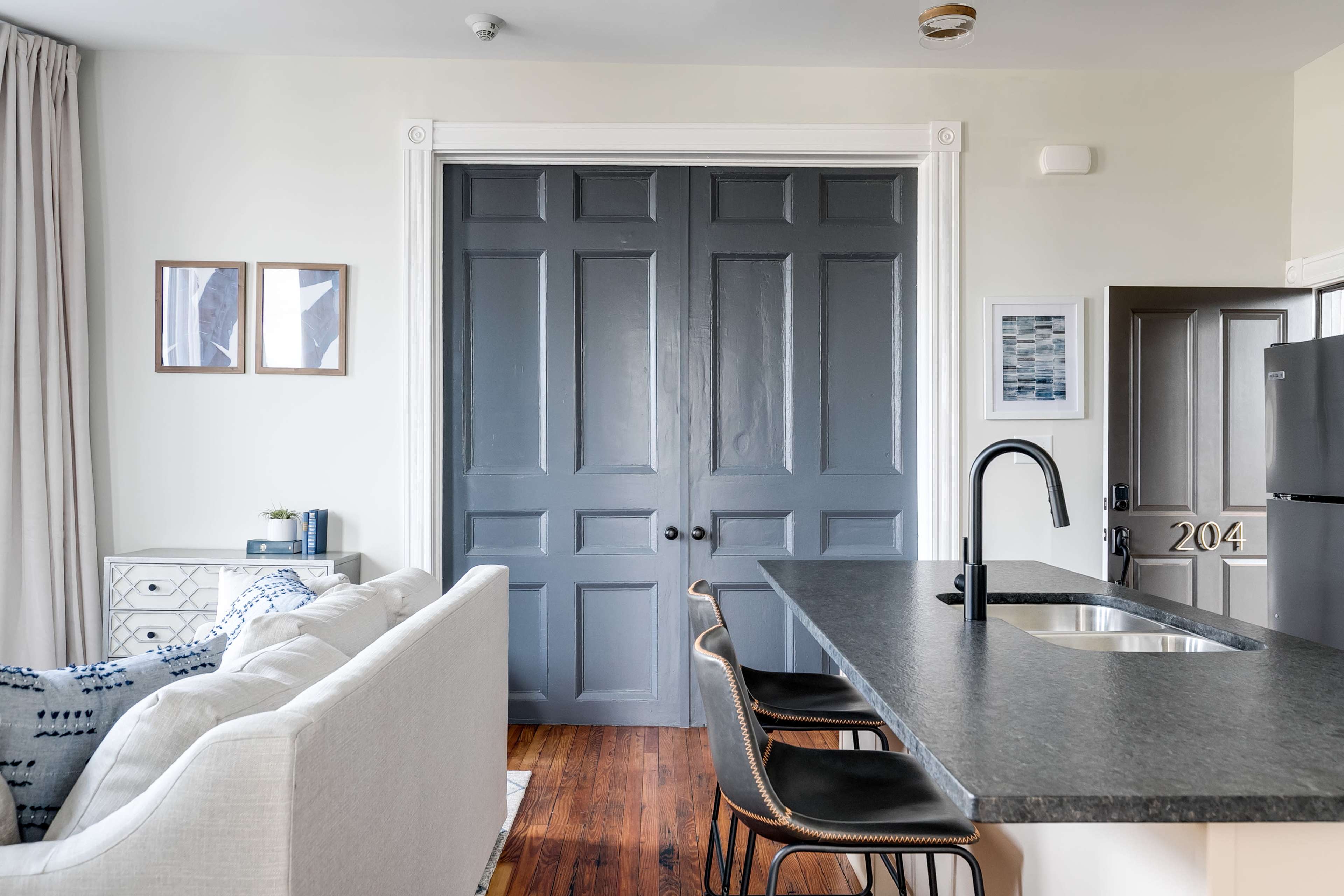 A modern kitchen and living area featuring a gray door, a white sofa, and a bar with three black stools.