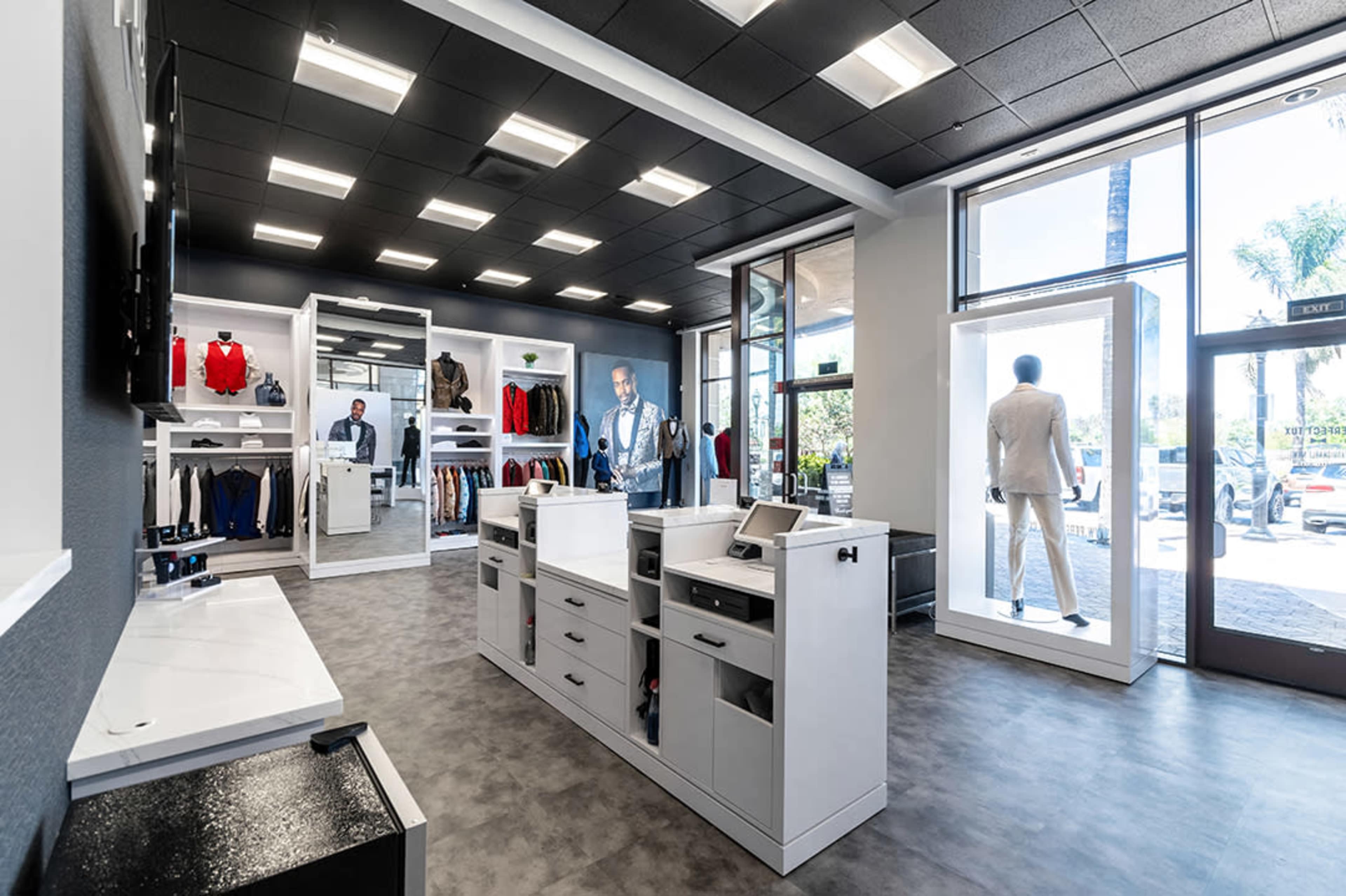 The interior of a clothing retail store featuring displays of men's suits and casual wear, alongside checkout counters.