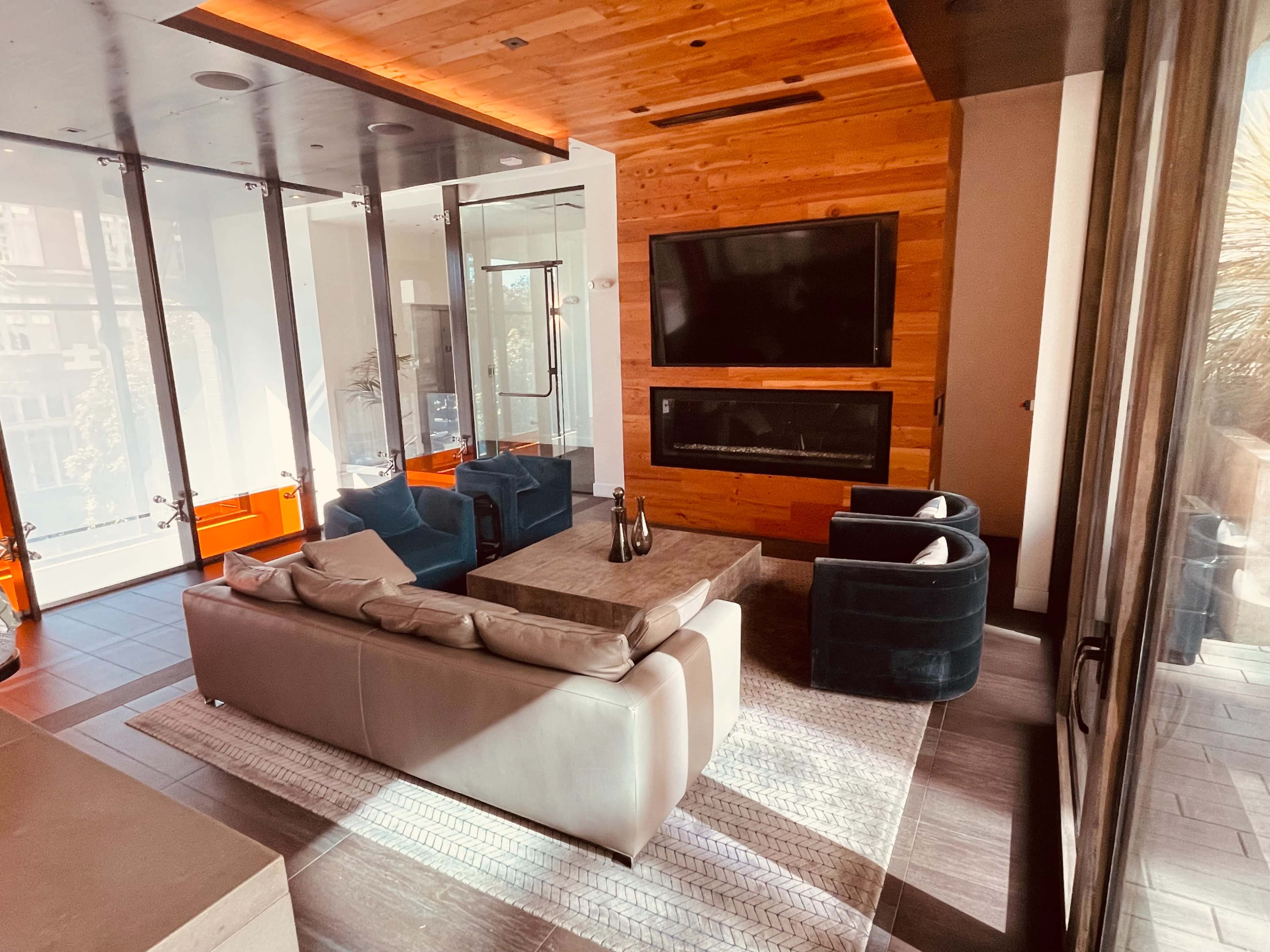 A modern living room featuring a sectional sofa, two armchairs, a coffee table, and a wall-mounted television above an electric fireplace.