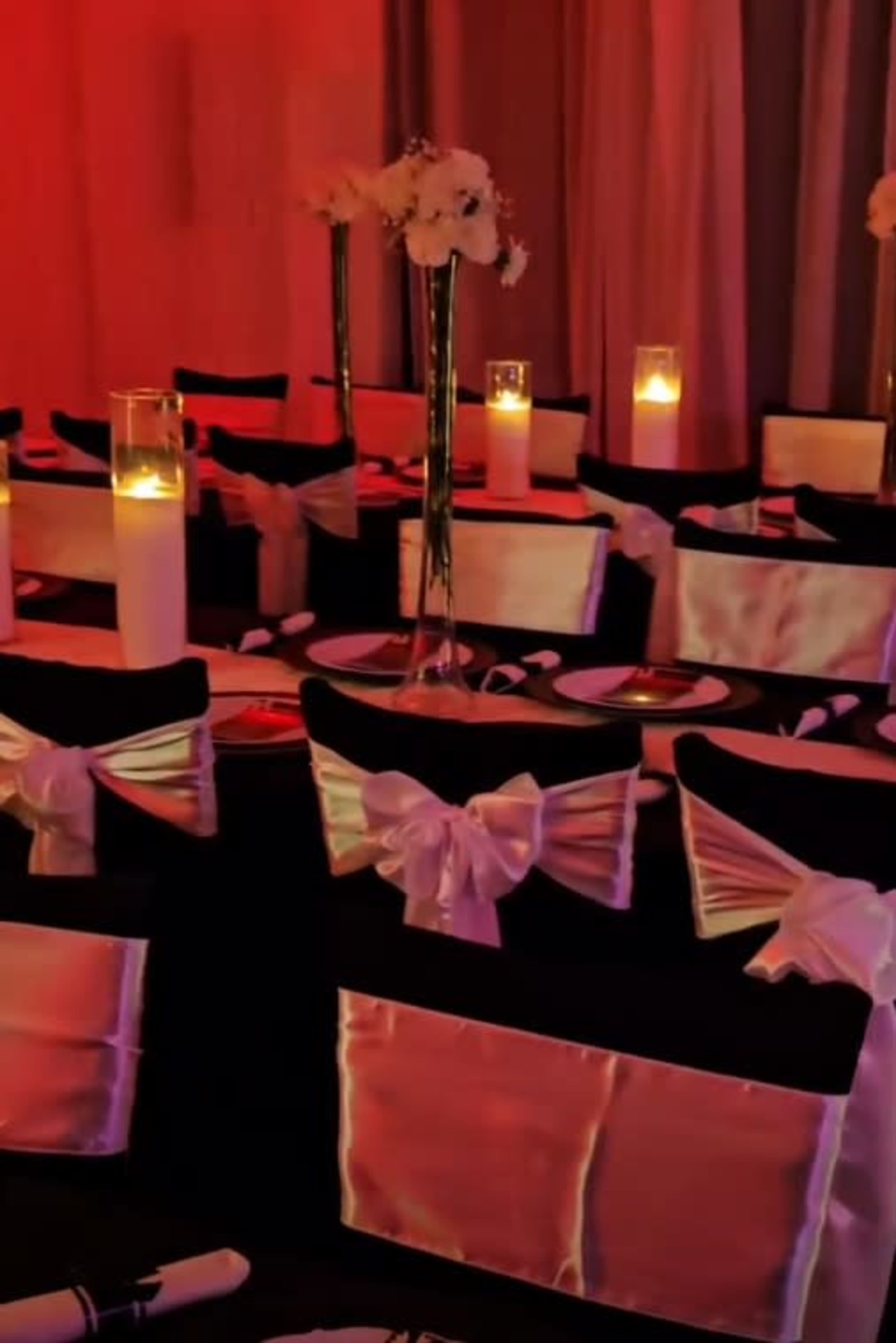 The image shows a banquet setup with black table covers adorned with white sashes, candles in glass holders, and floral arrangements on the tables.