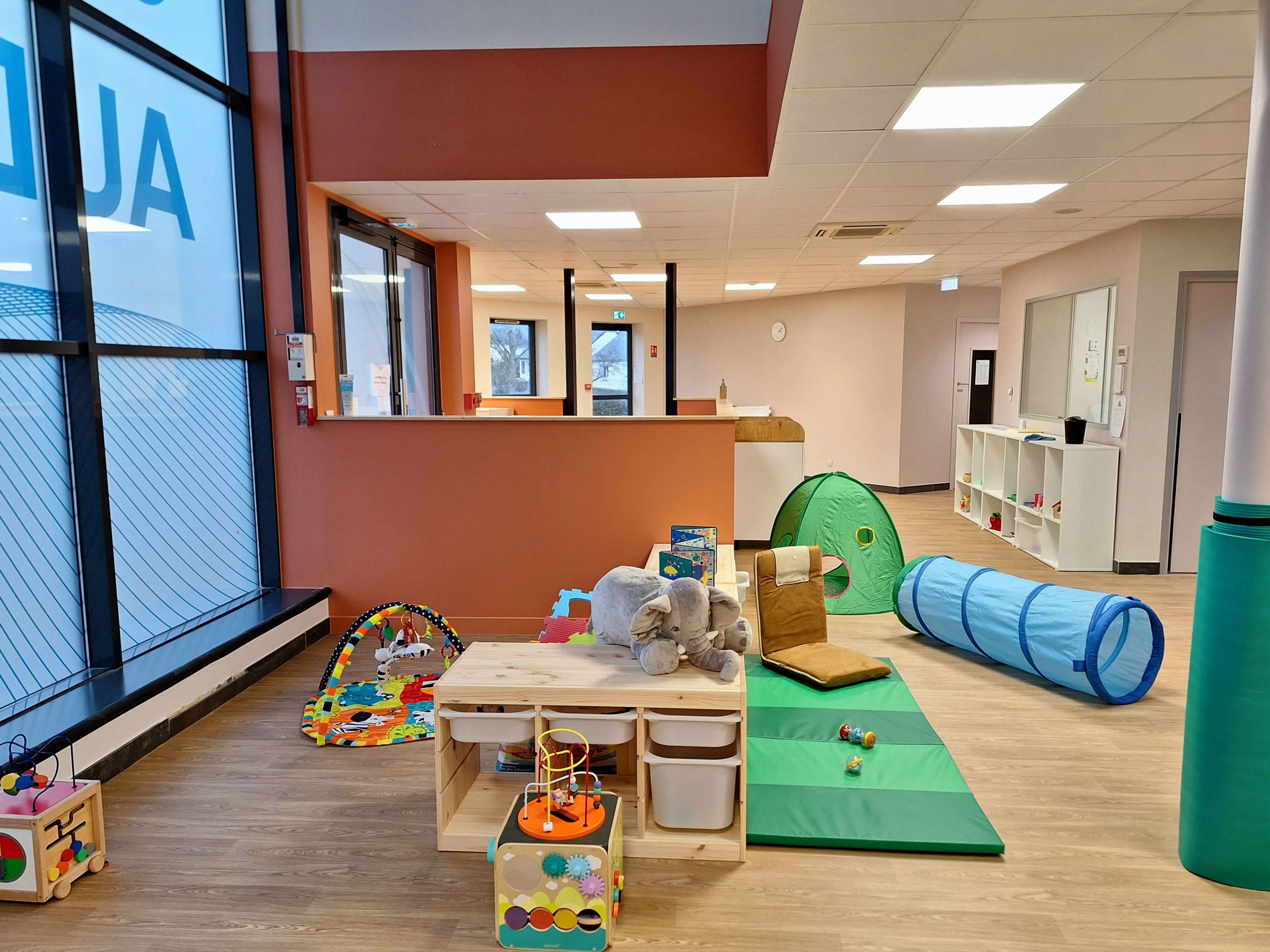 The image shows an indoor play area filled with colorful toys, soft mats, and a tunnel for children.
