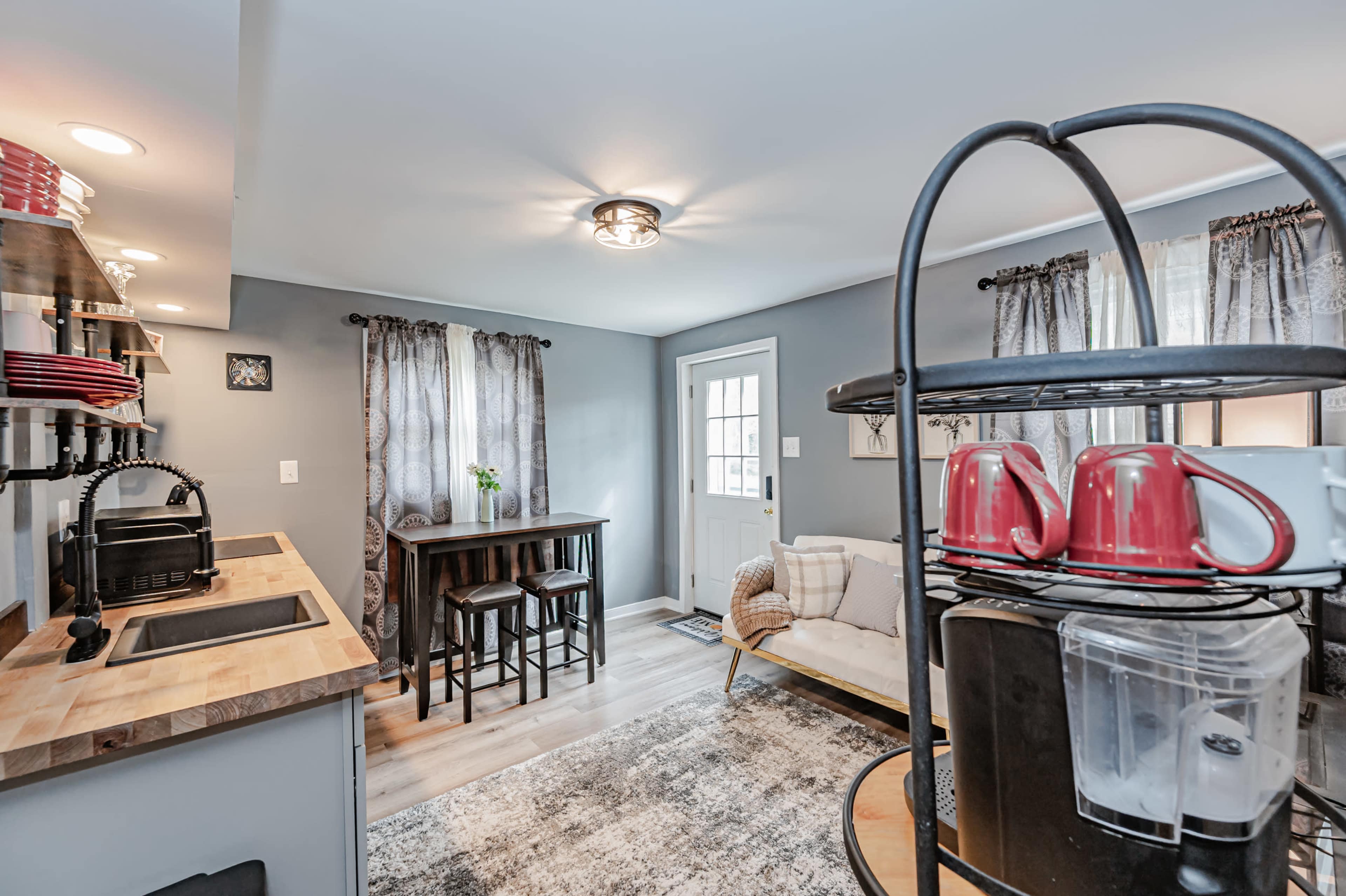 A compact kitchen and living area featuring a small dining table with two stools, a couch, and kitchen appliances on a wooden countertop.