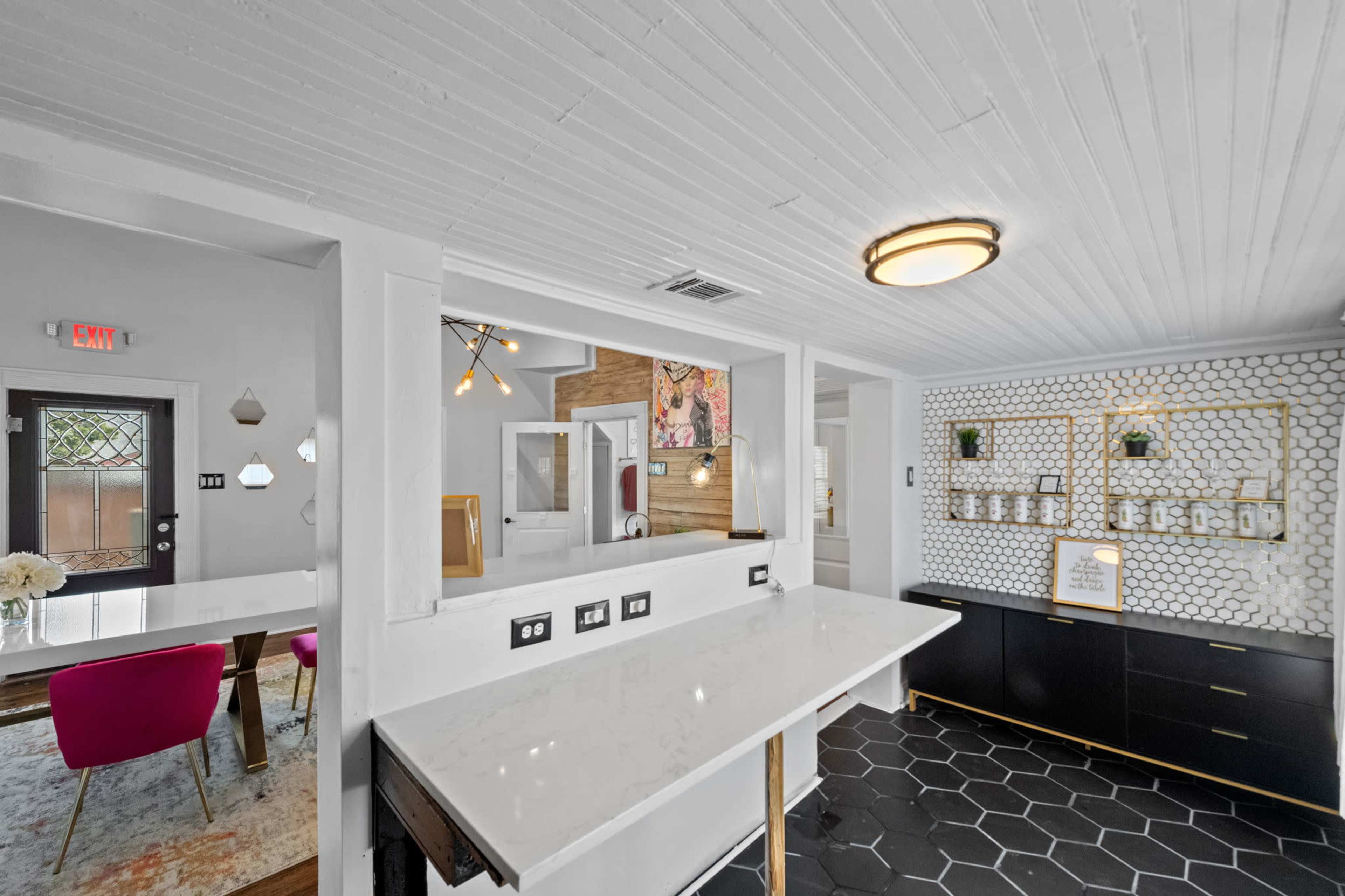 A modern interior space with a white countertop, black cabinetry, and a hexagonal tile floor, seamlessly connecting a dining area to a well-lit room.