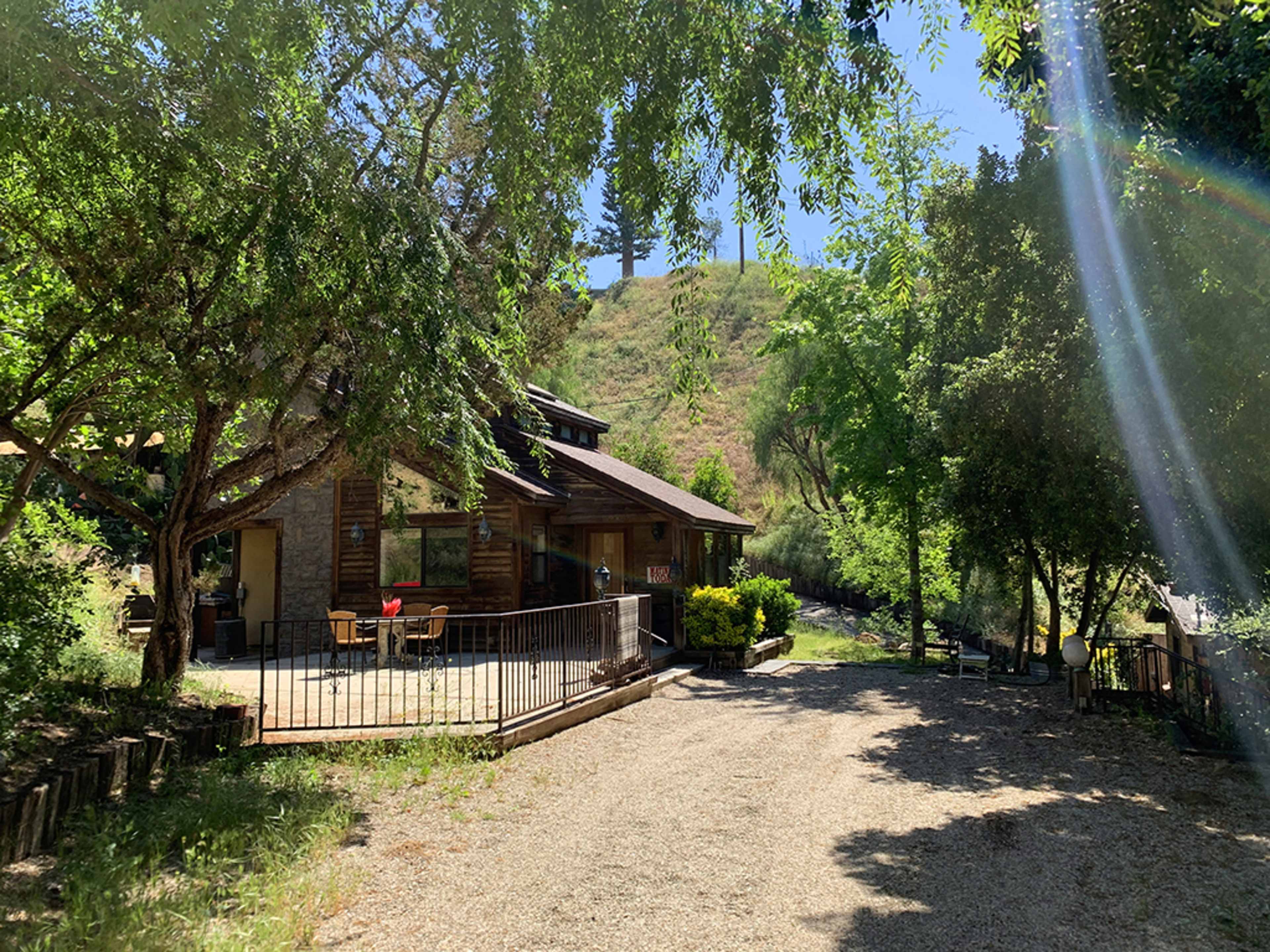 A gravel pathway leads to a wooden house surrounded by trees and hillside.
