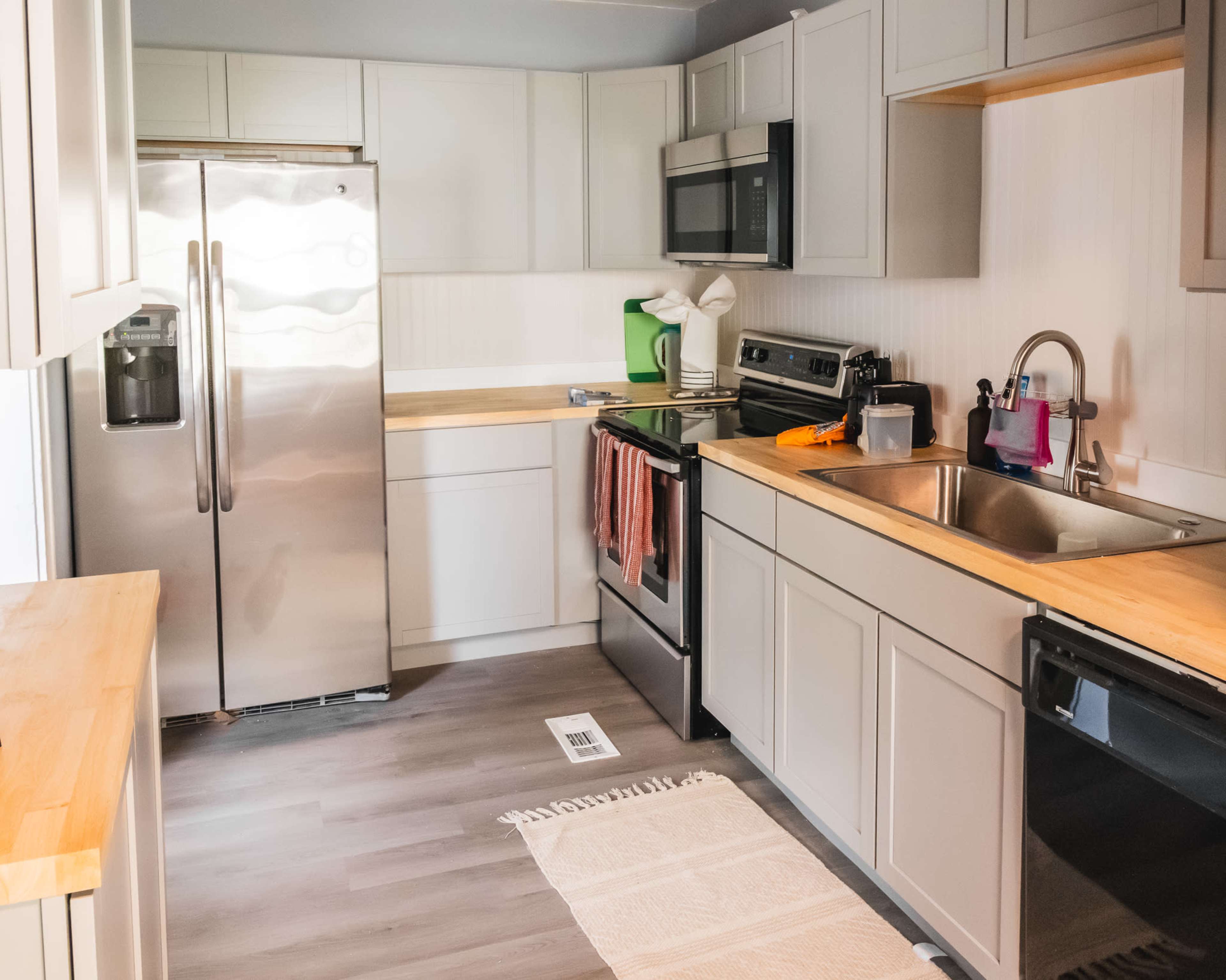 A modern kitchen features stainless steel appliances, light gray cabinets, and a wooden countertop.