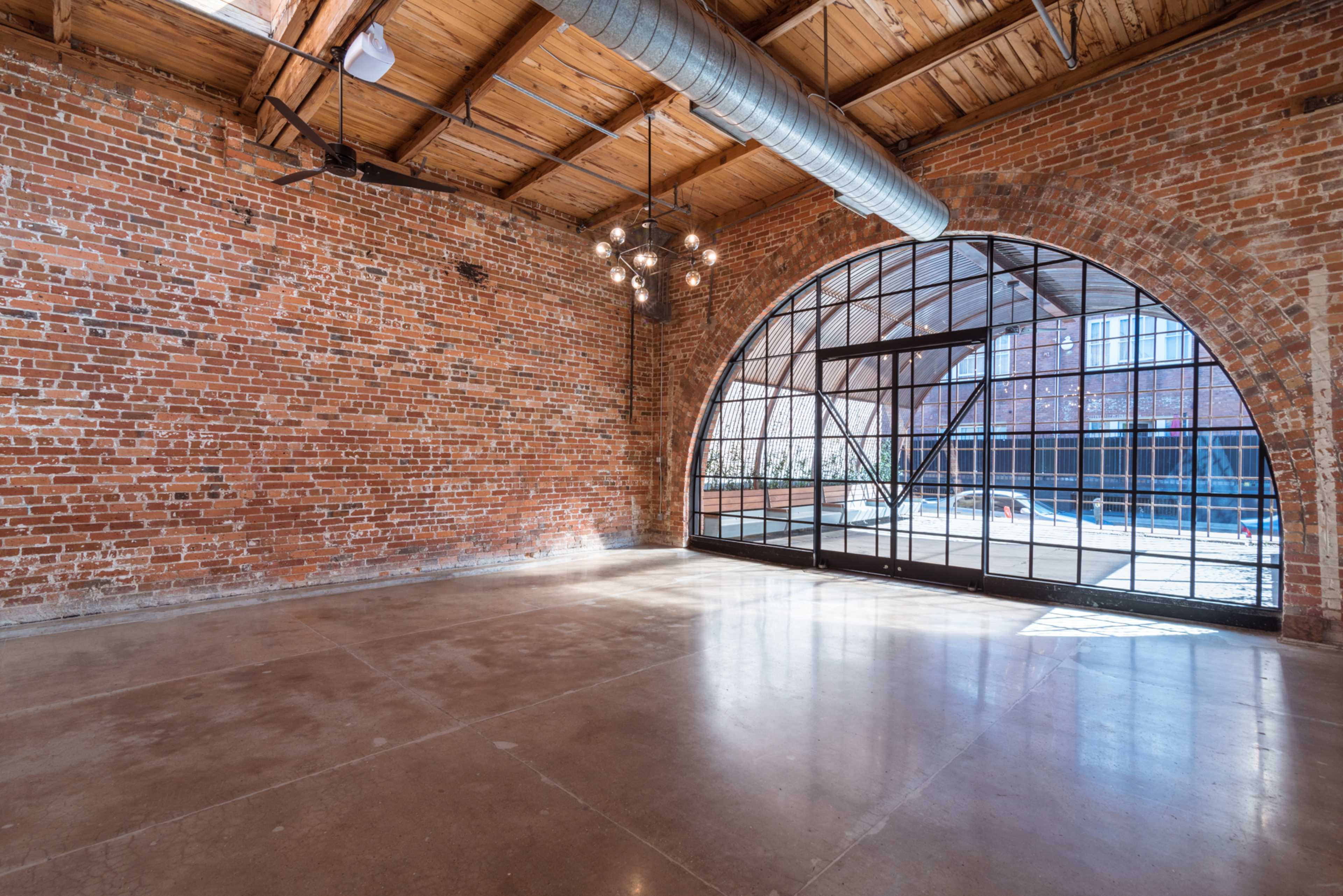 An industrial-style interior with exposed brick walls, a large arched window, and polished concrete flooring.
