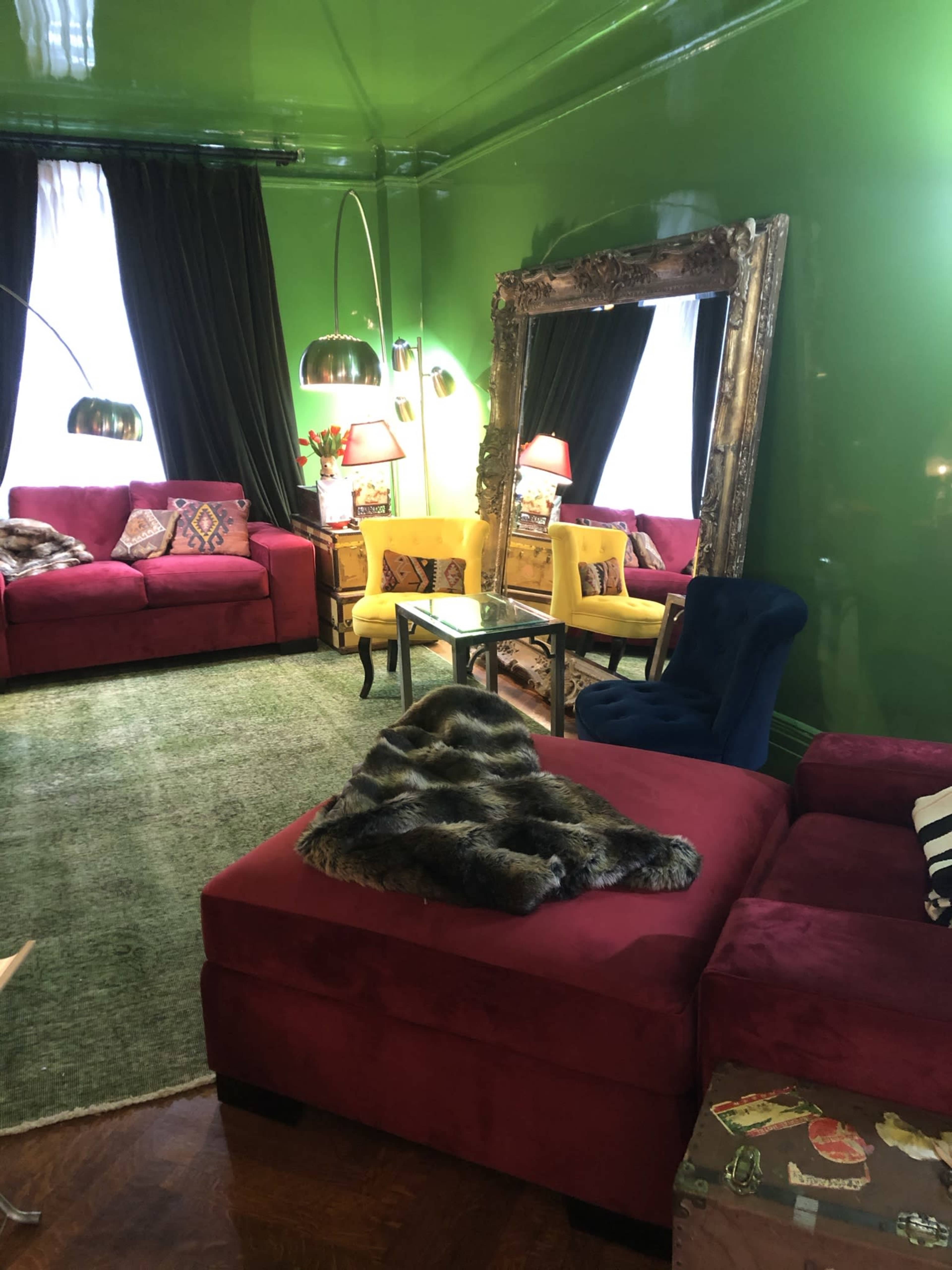 A vibrant living room with green walls, a plush rug, and a mix of red and yellow upholstered furniture.