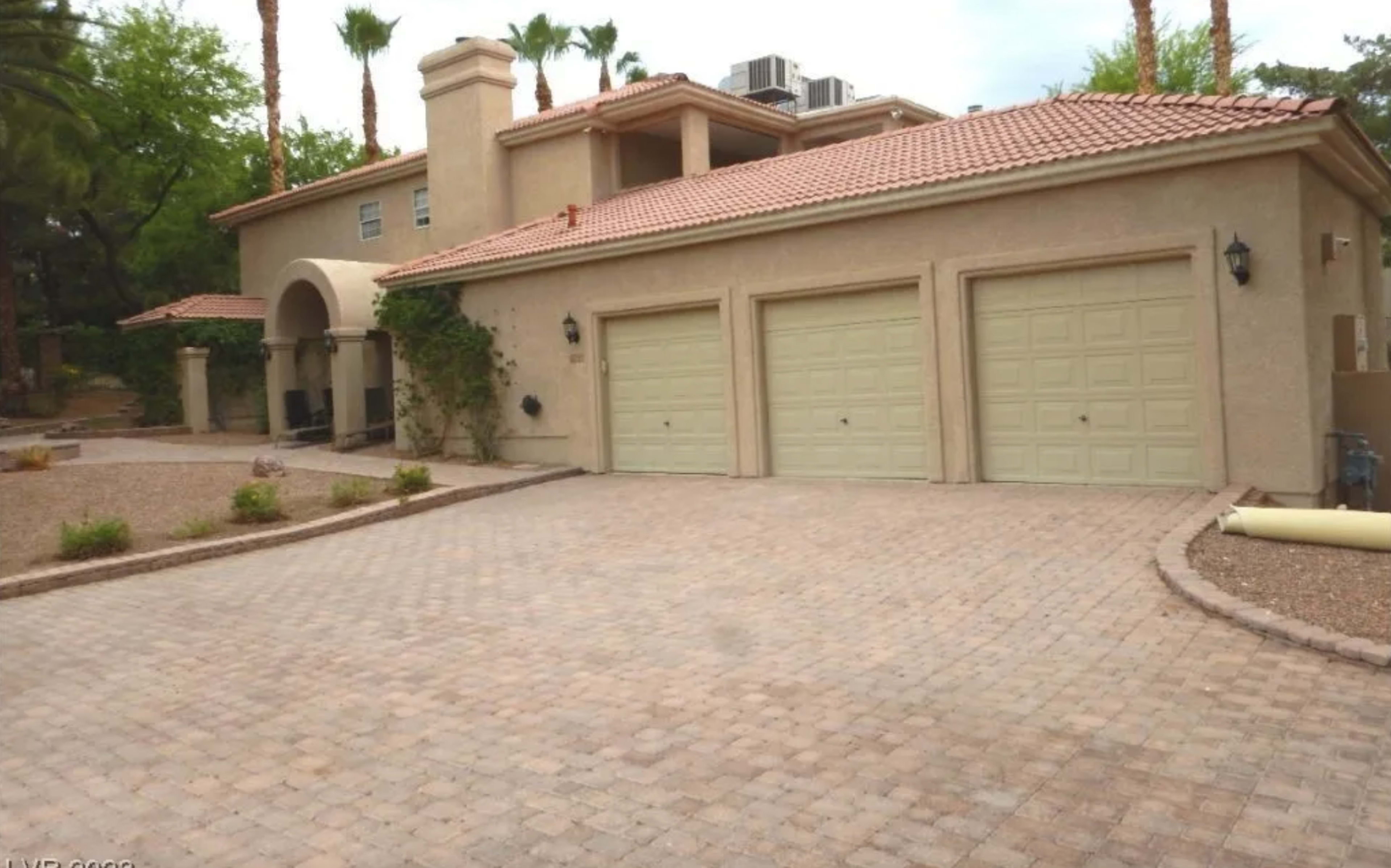 A two-story house with three garages, surrounded by palm trees and a paved driveway.