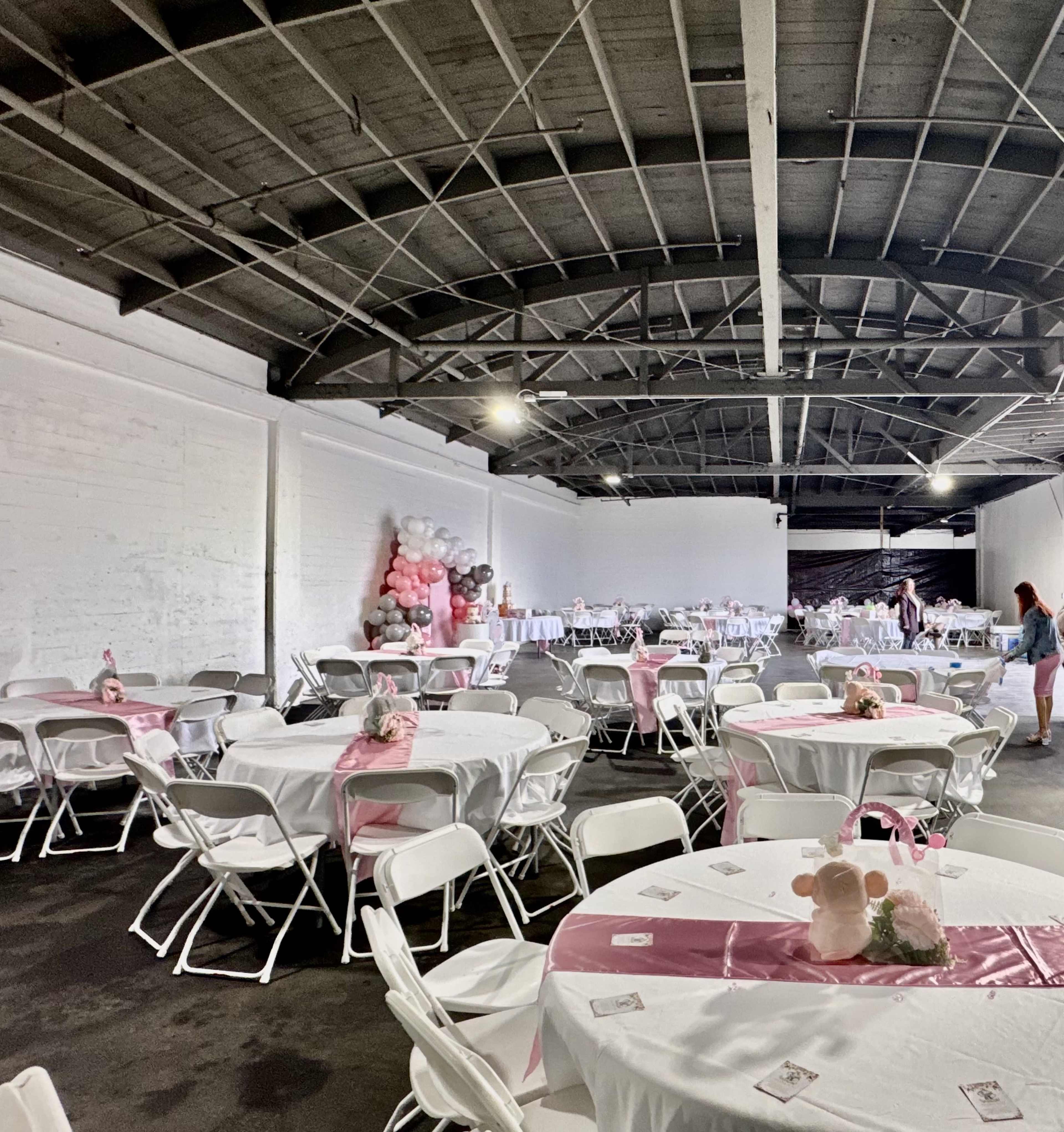 The image shows a large event space with rows of round tables covered in pink tablecloths and decorated with floral centerpieces.