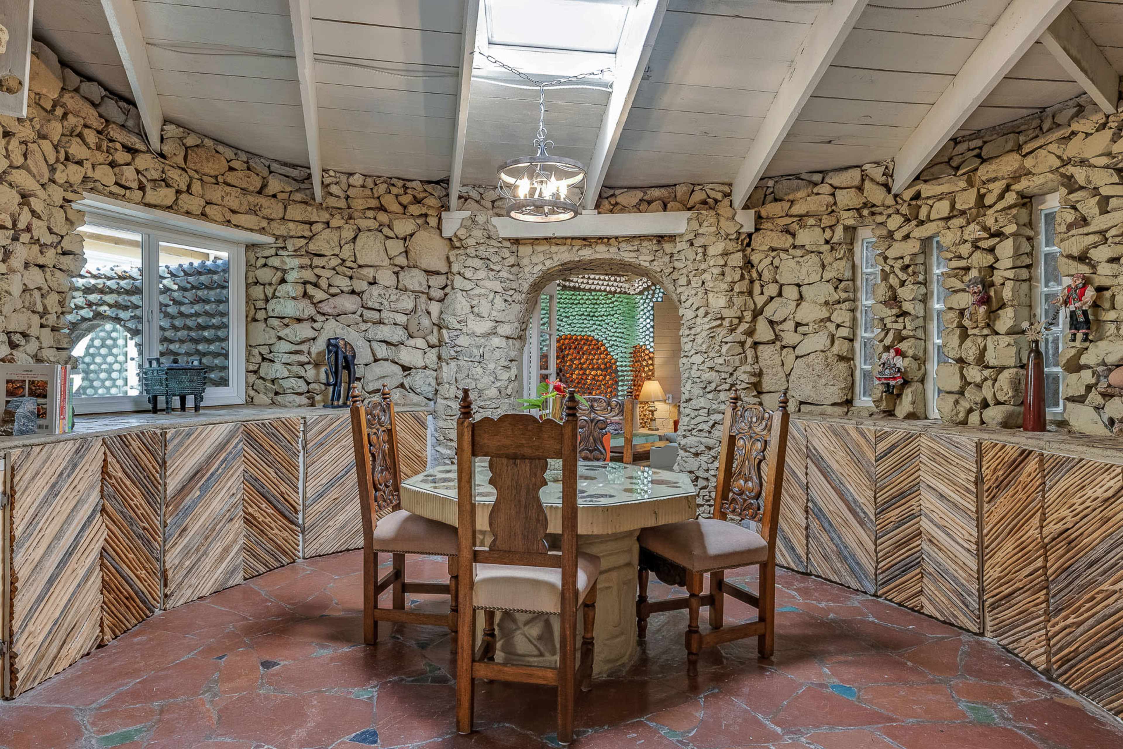 The image shows a circular dining area with a stone wall, wooden furniture, and a skylight above.
