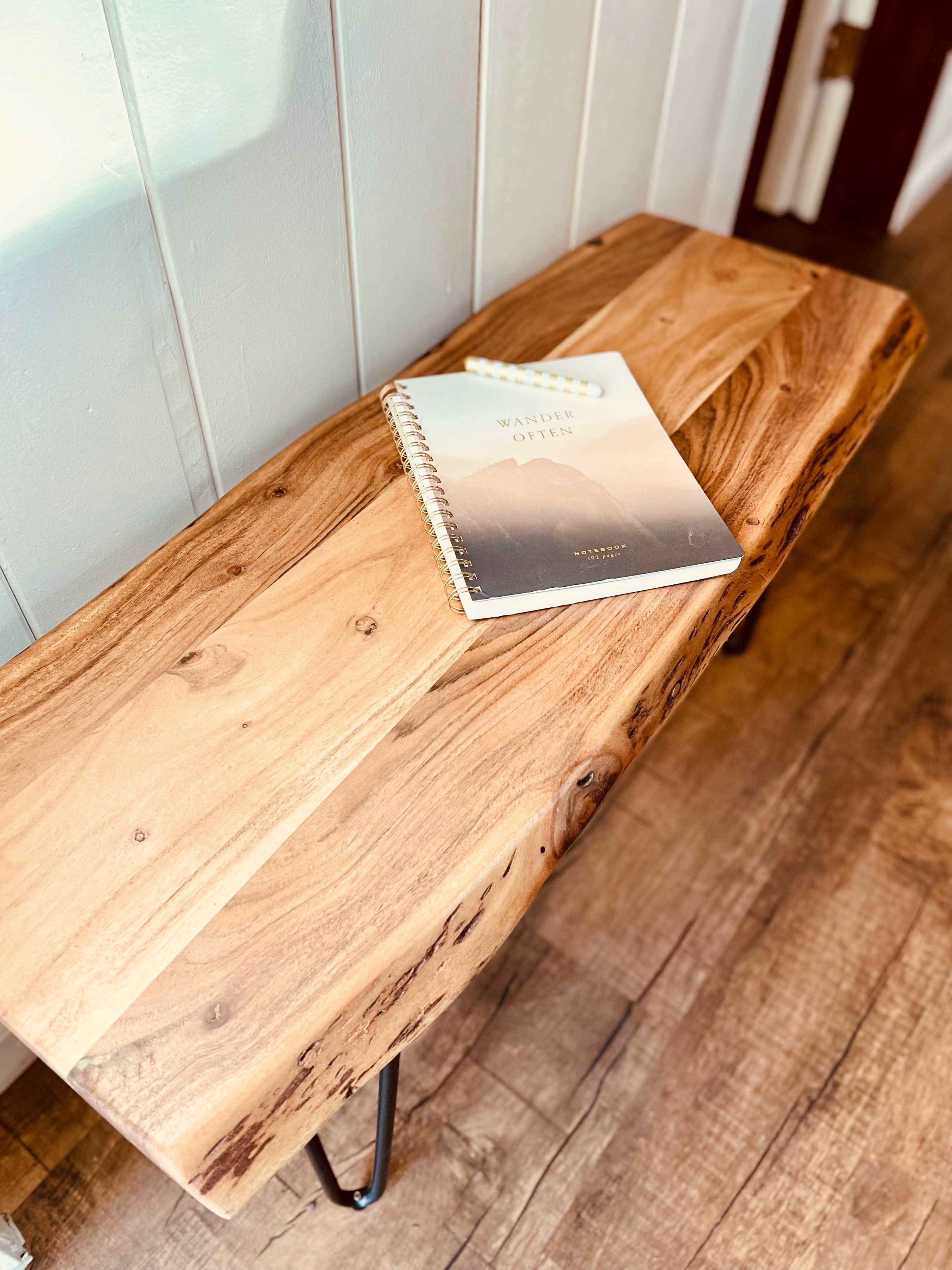 A wooden bench with a spiral-bound notebook titled "Walden" rests on its surface, set against a white wall.