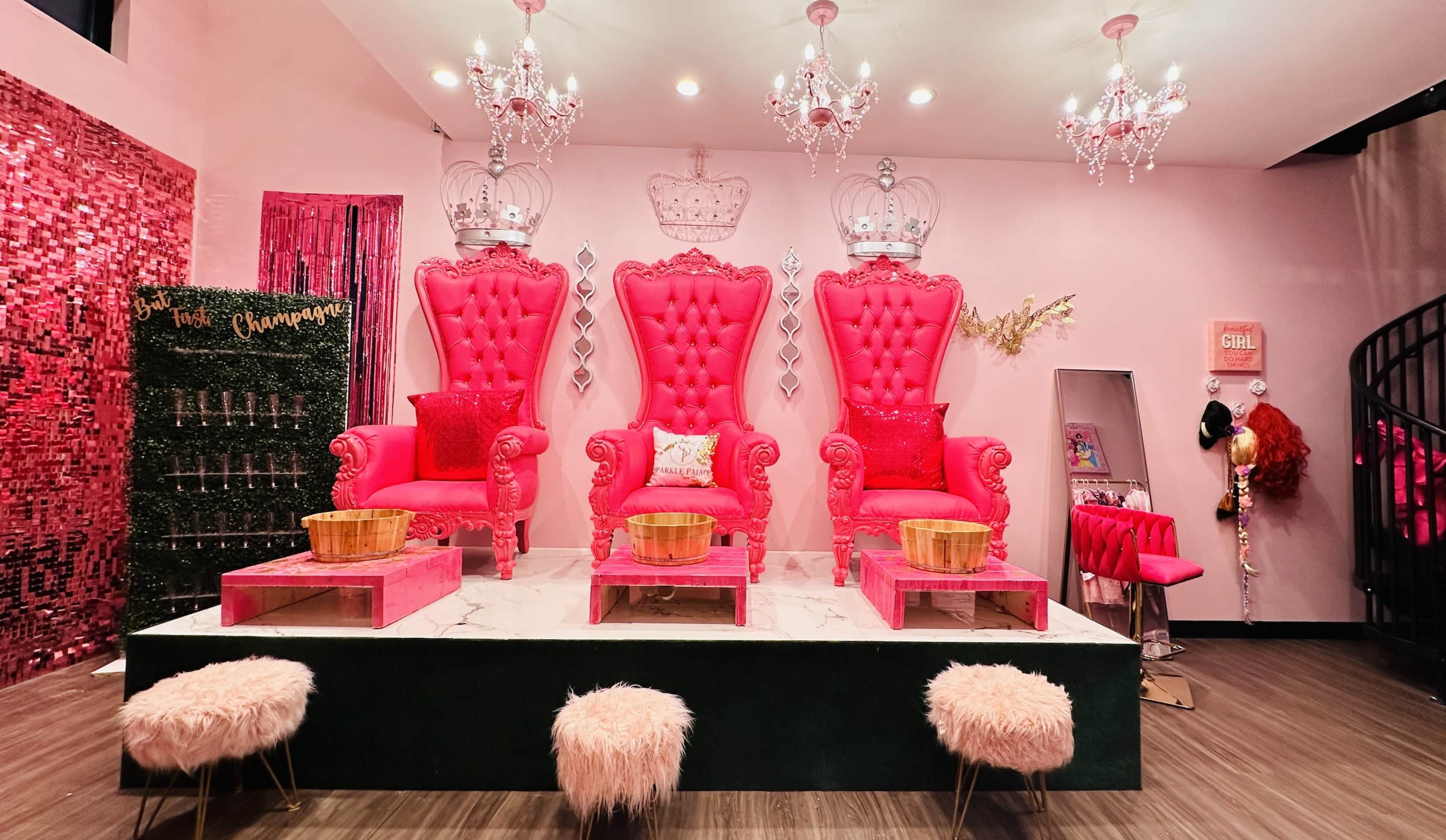 A vibrant pink room featuring three ornate, high-backed chairs with crowns, surrounded by decorative elements like chandeliers and plush seating.
