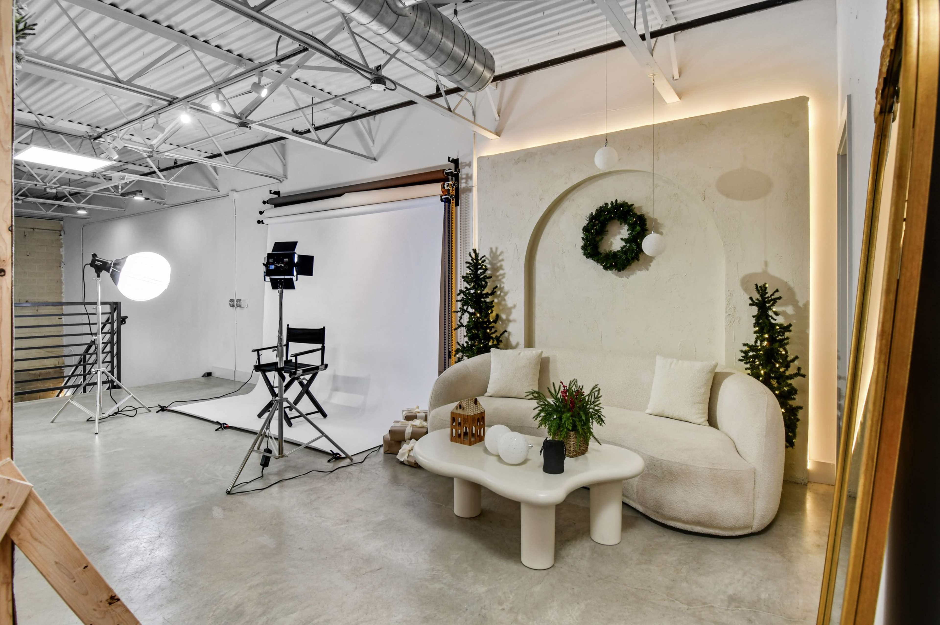The image shows a modern photo studio featuring a curved sofa, a white backdrop for shooting, and decorative elements like small trees and a wreath.